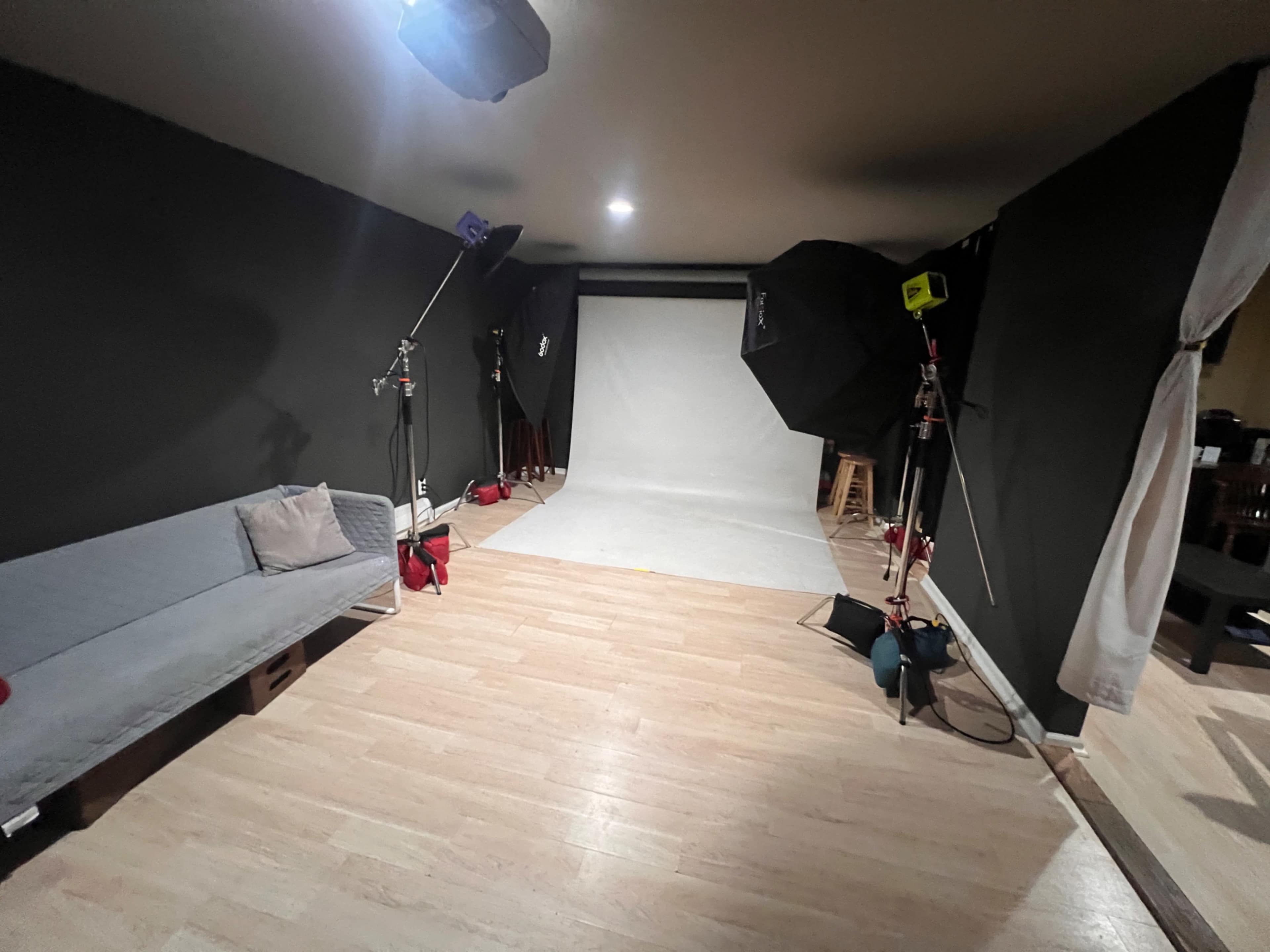 A photography studio with a backdrop and lighting equipment set up, along with a gray couch in one corner of the room.