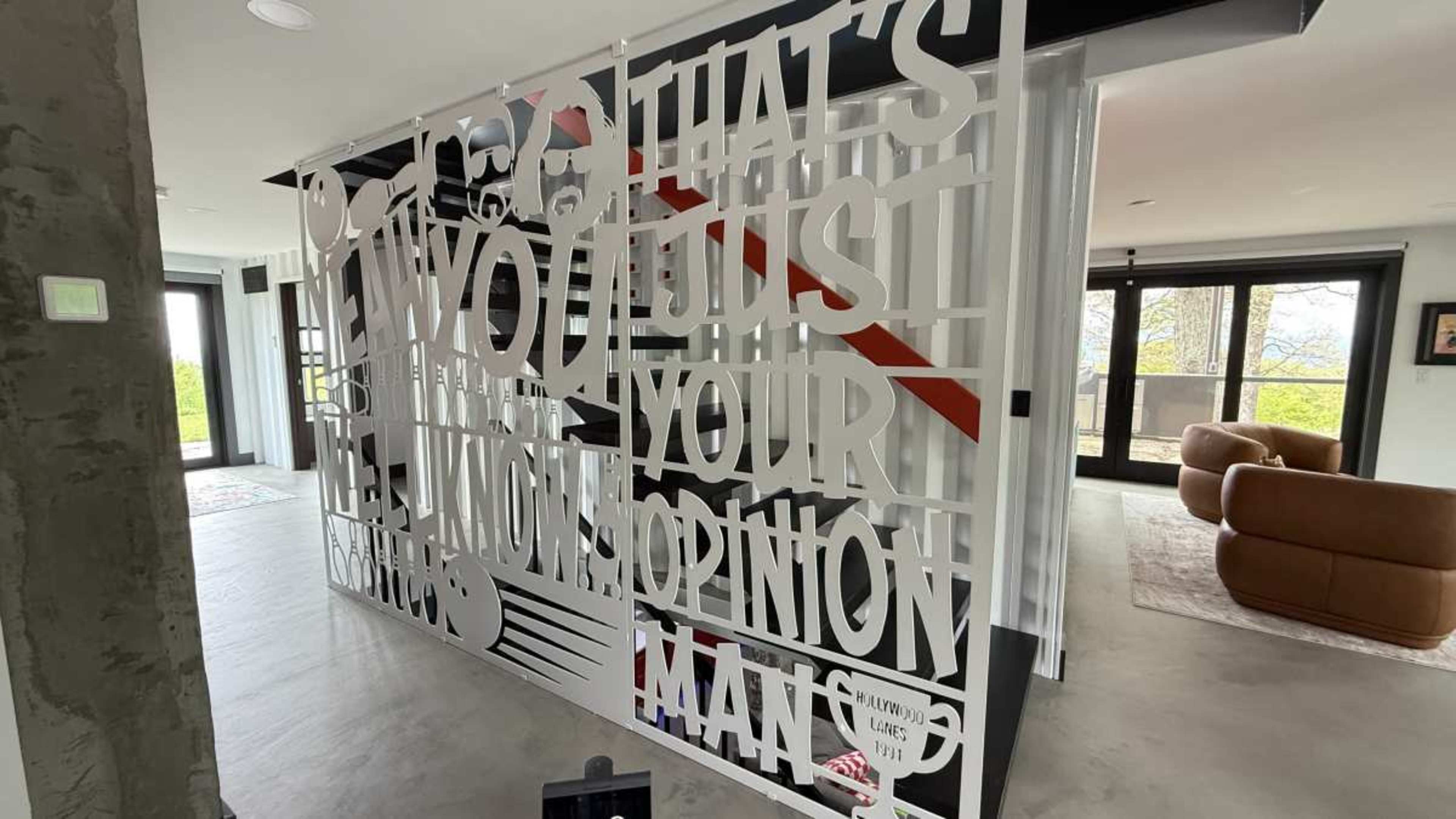 The image shows a modern interior space featuring a decorative partition wall with oversized text and graphic elements.