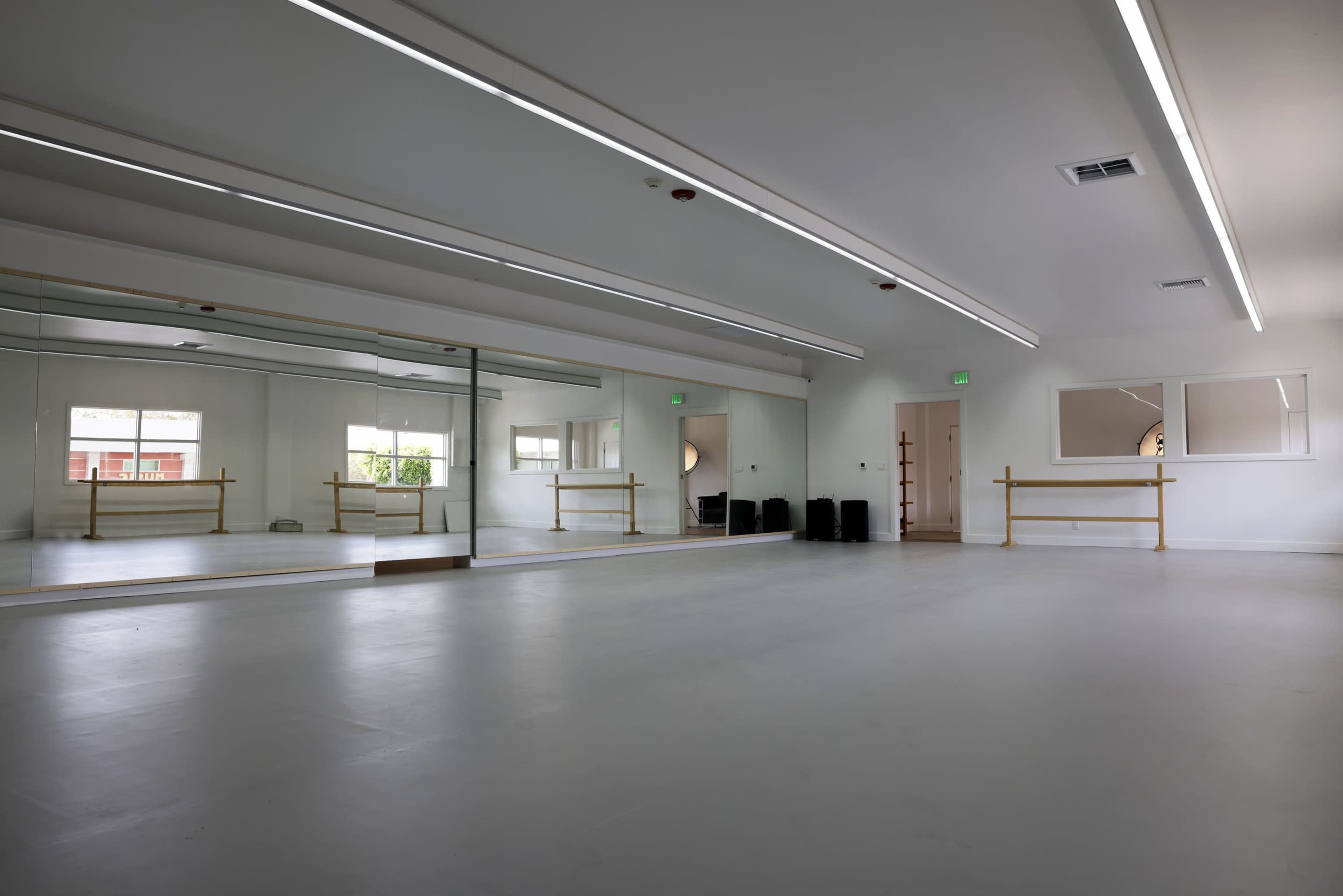 A spacious dance studio with mirrored walls, overhead lighting, and a ballet barre along one side.