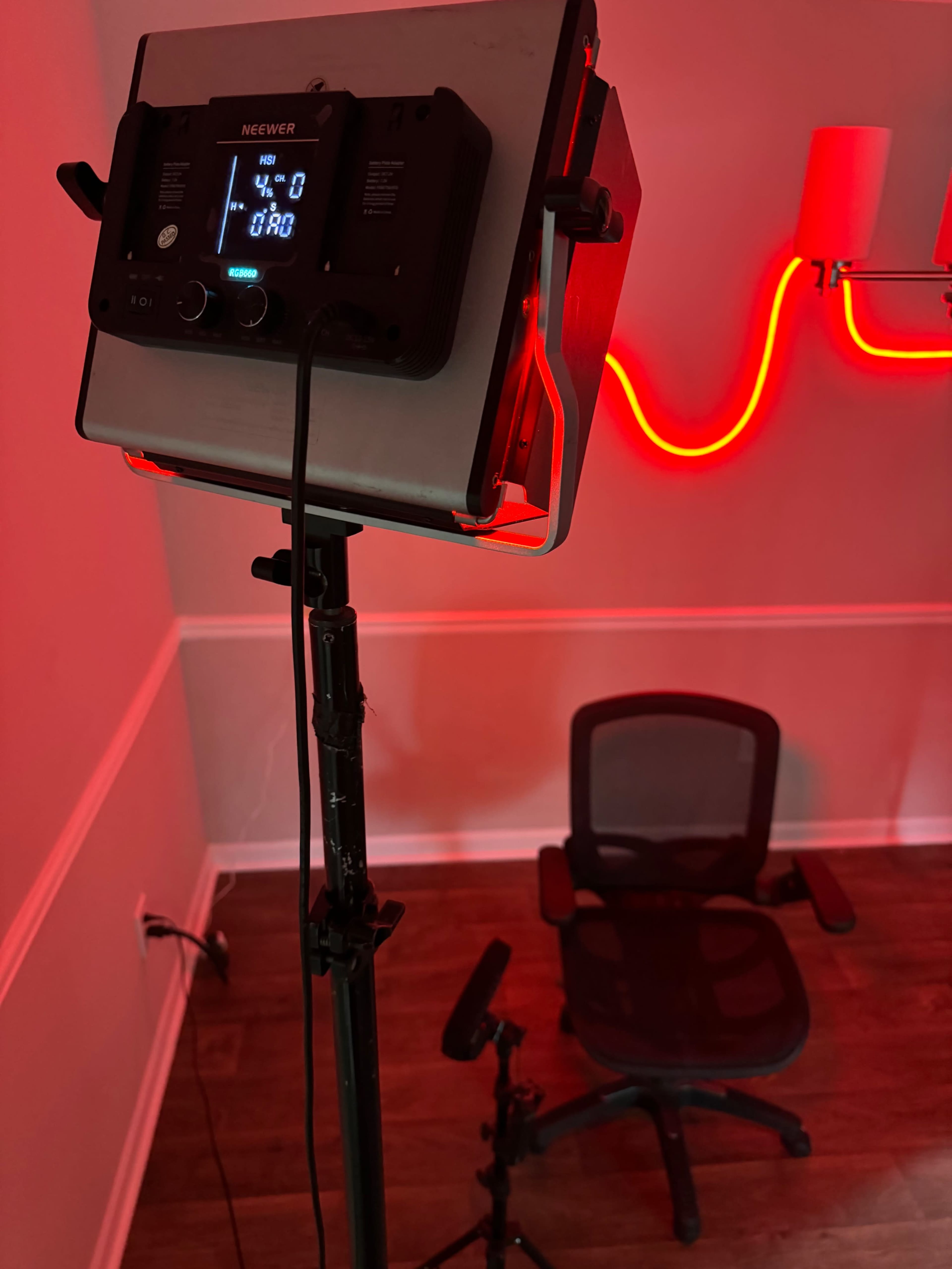 A mounted light fixture is positioned above an empty office chair in a room with a red illuminated wall.