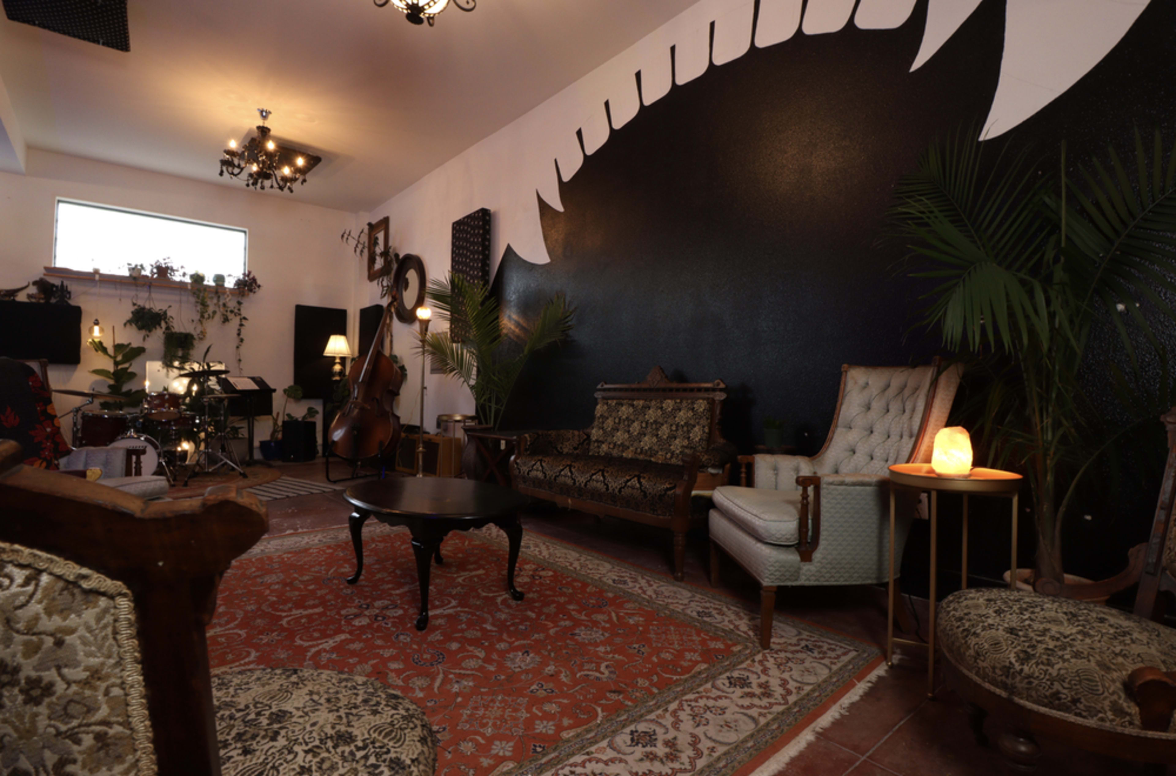 A cozy music studio featuring vintage furniture, a decorative rug, and a large black mural with a stylized design on the wall.