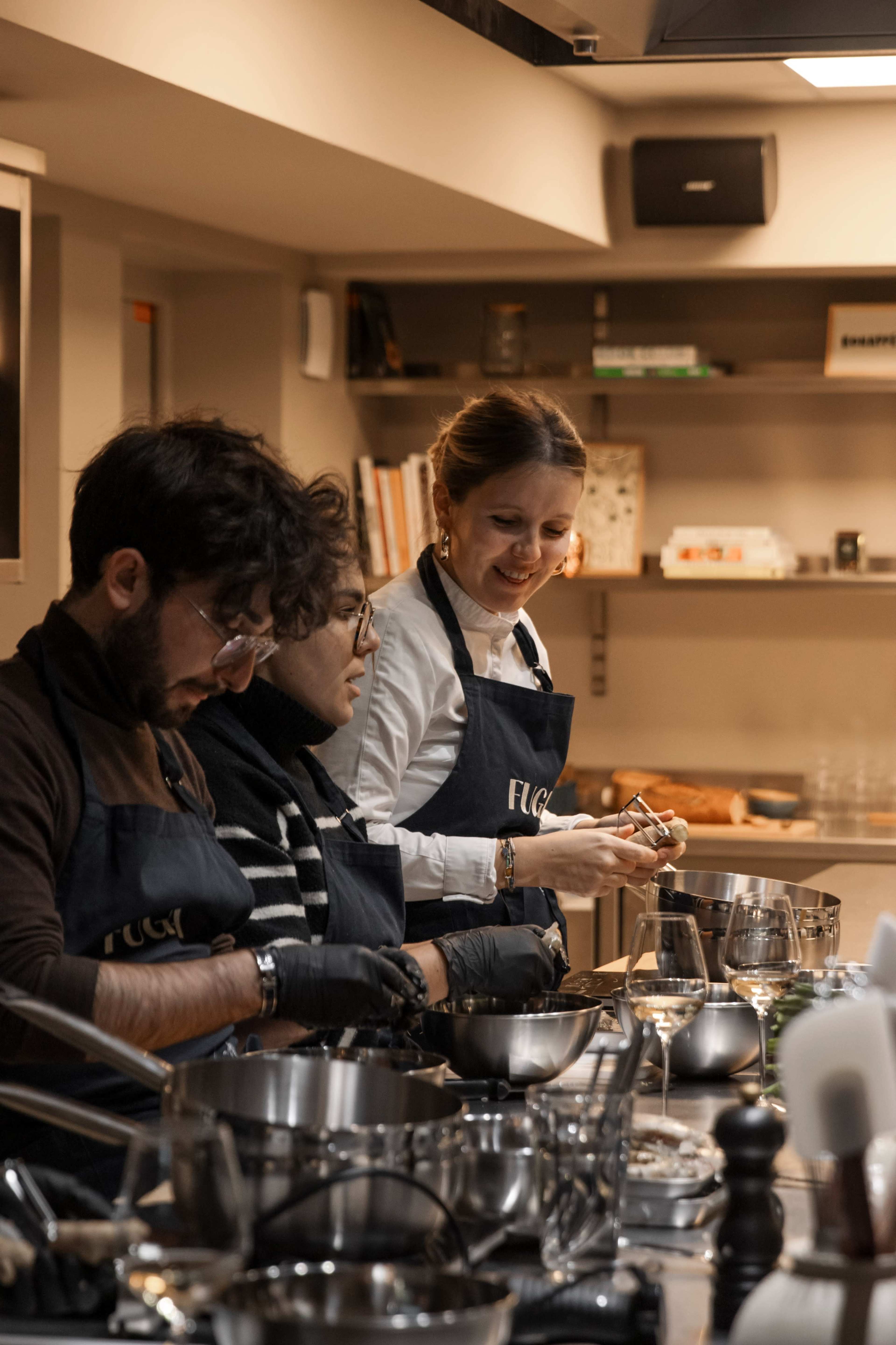 Three individuals work together in a kitchen, focusing on food preparation while wearing matching dark aprons.
