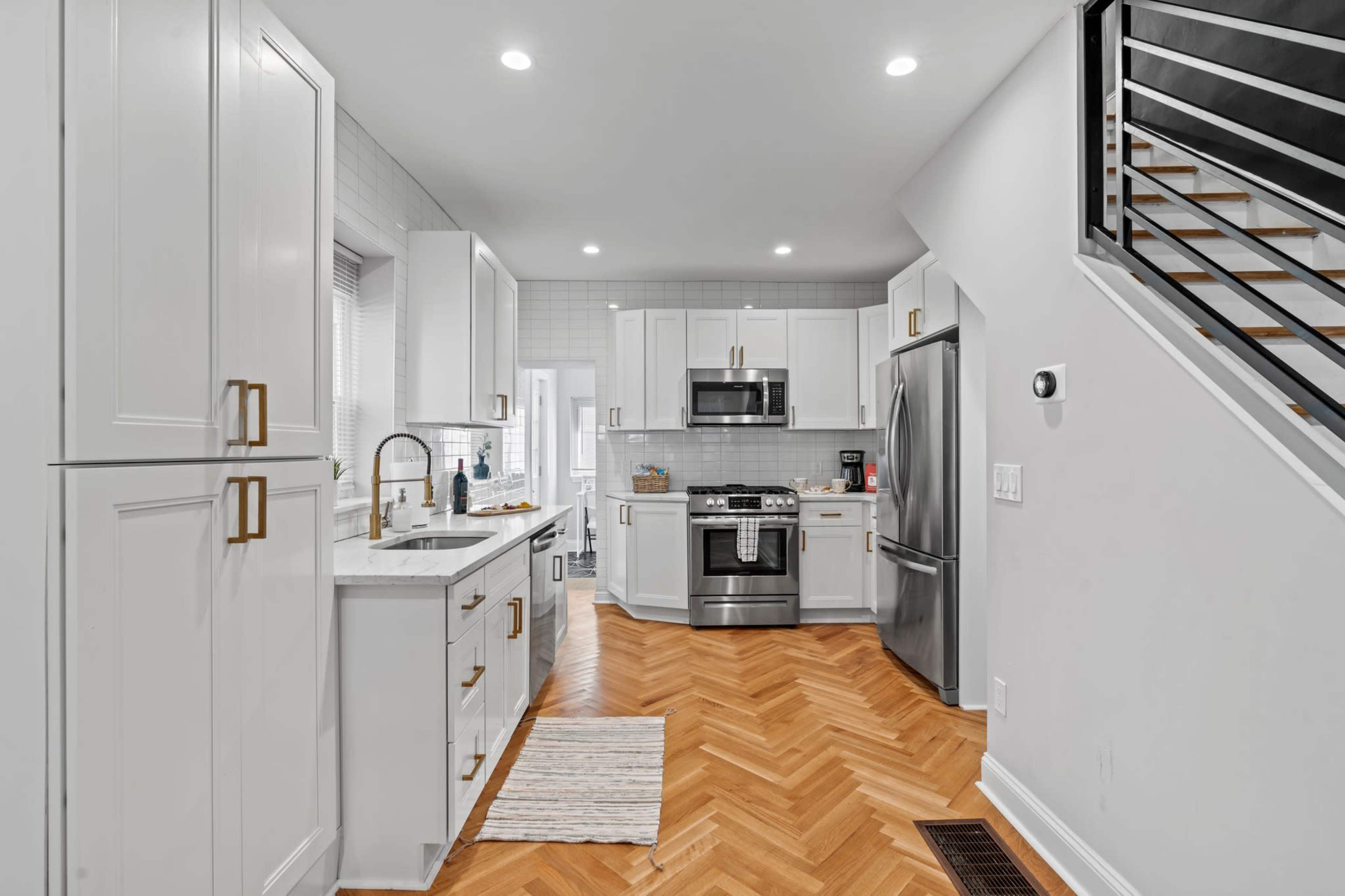 A modern kitchen features white cabinetry, stainless steel appliances, and herringbone-patterned hardwood flooring.