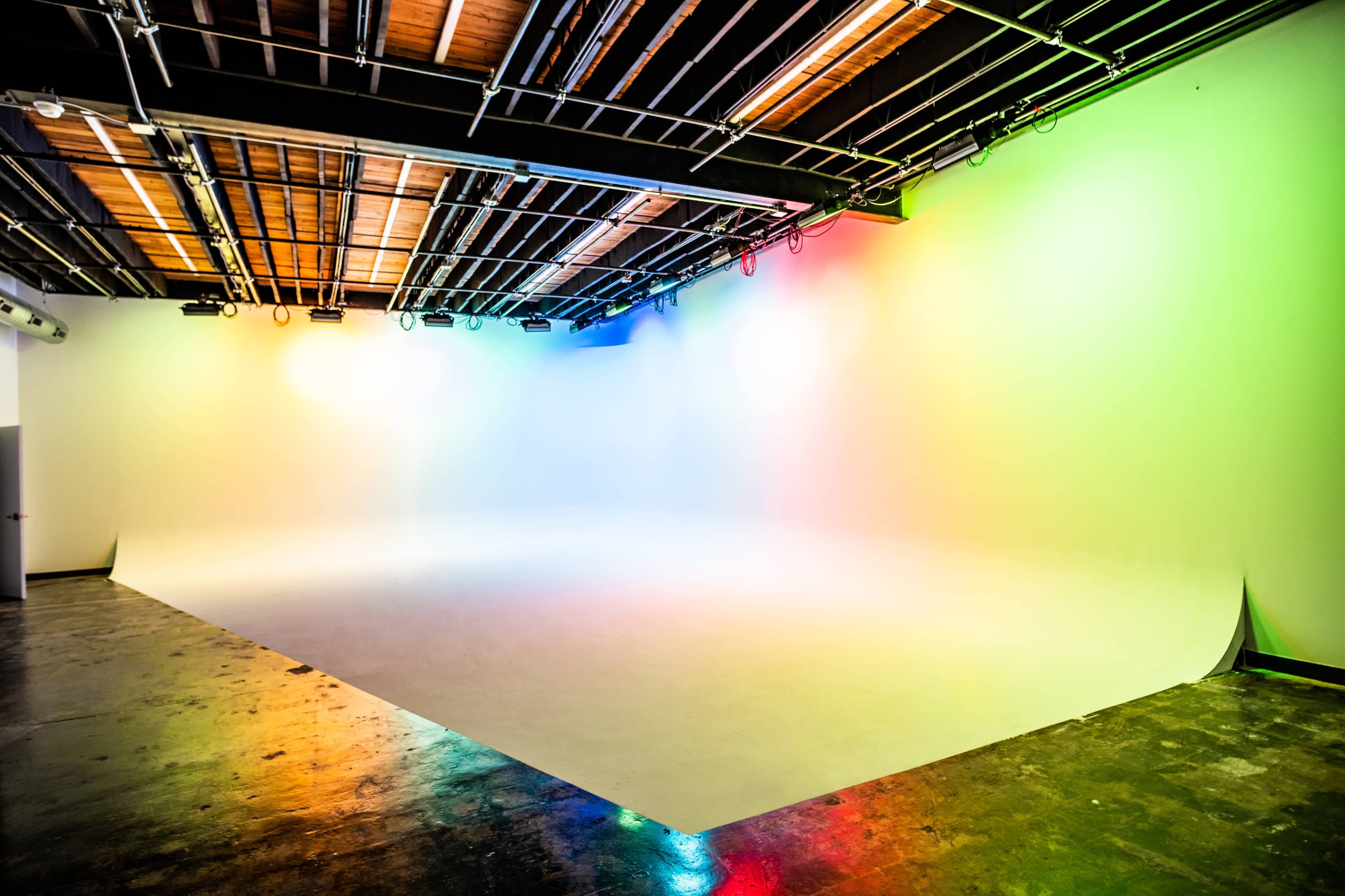 A spacious, empty studio with a seamless backdrop and colored lights illuminating the walls.