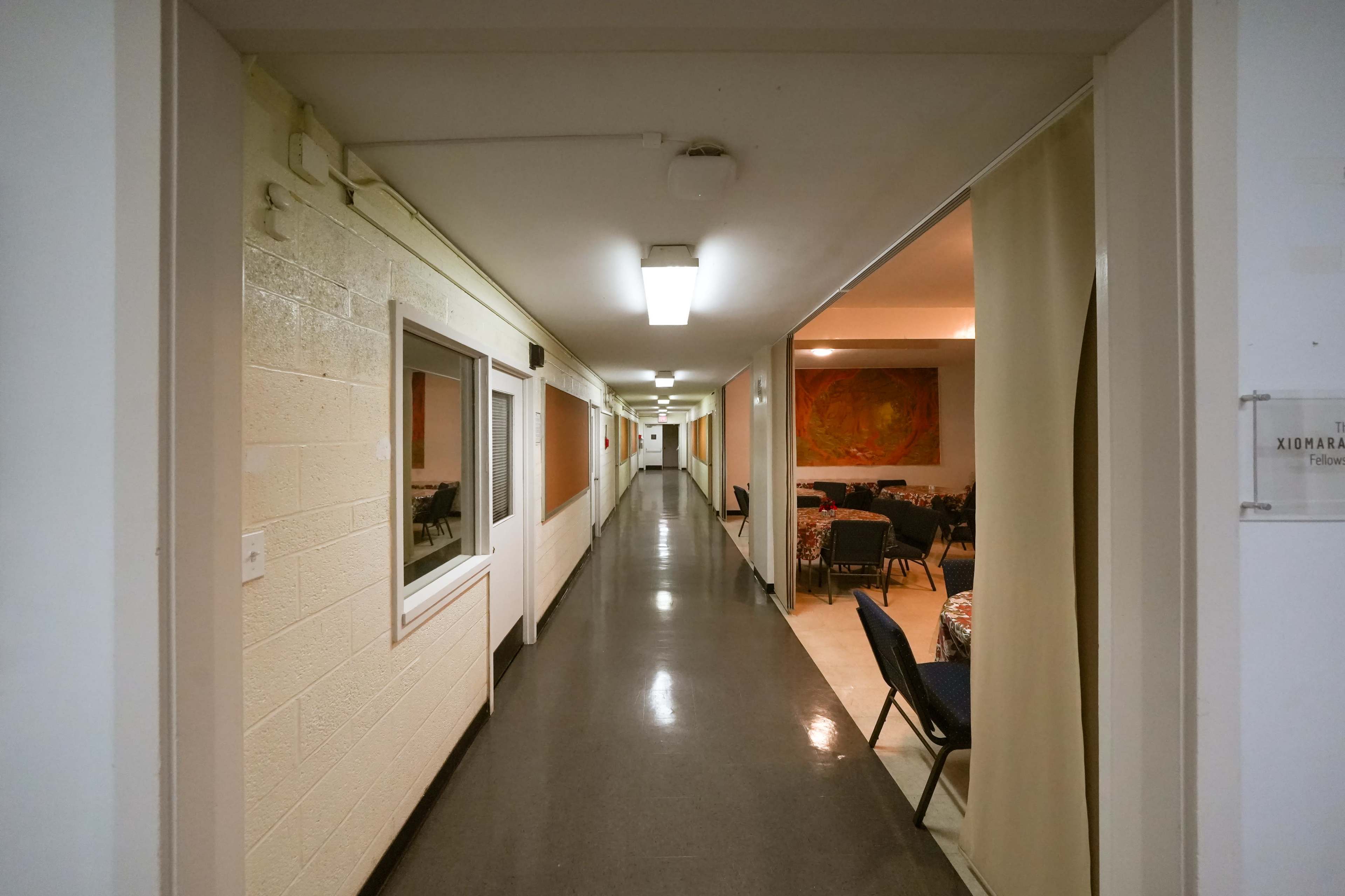 A long, narrow hallway with white walls and a shiny floor, leading to a dining area at the end.
