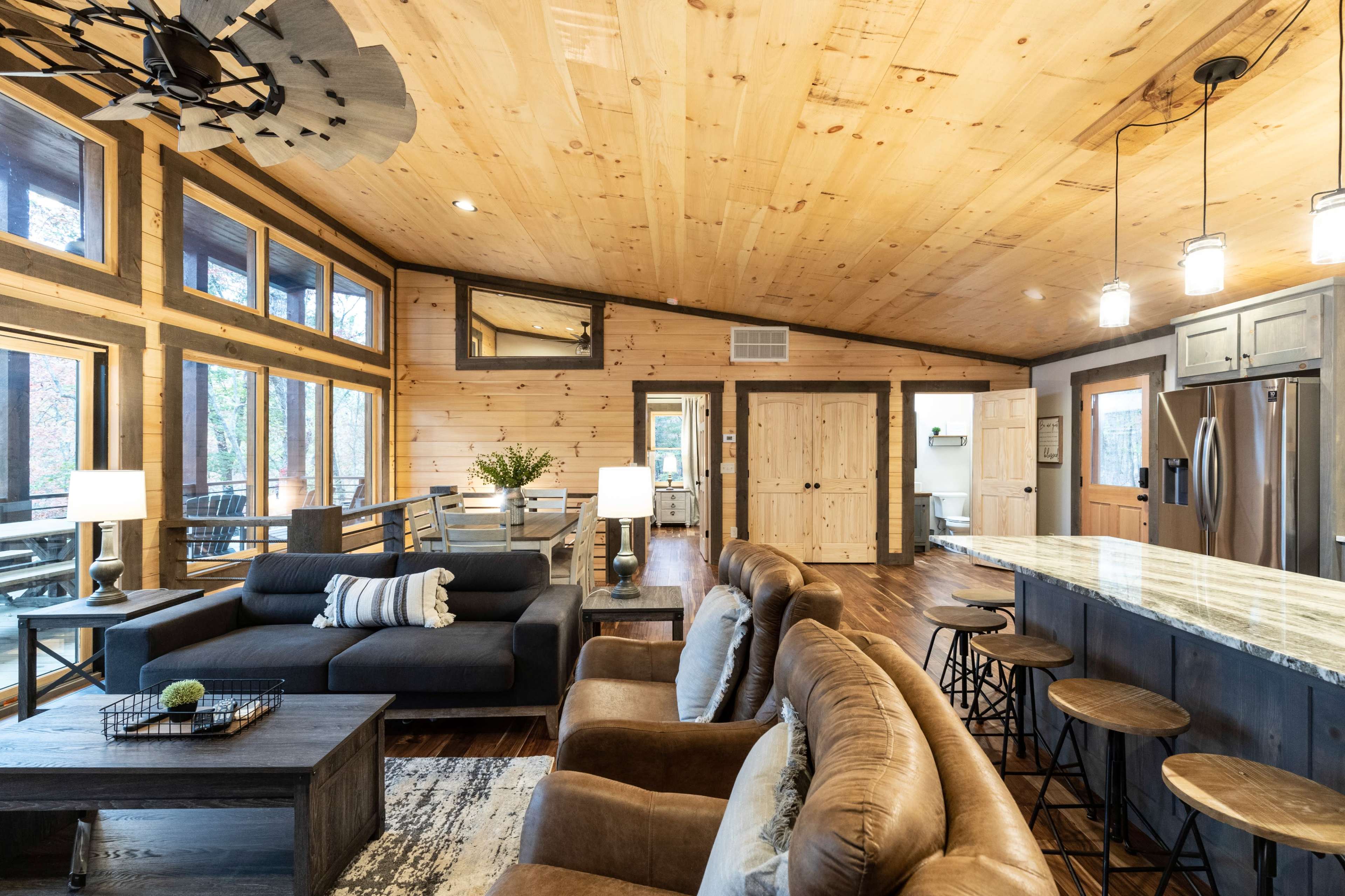 A spacious cabin-style interior with wooden walls, a modern kitchen island, and a mix of comfortable seating arrangements.