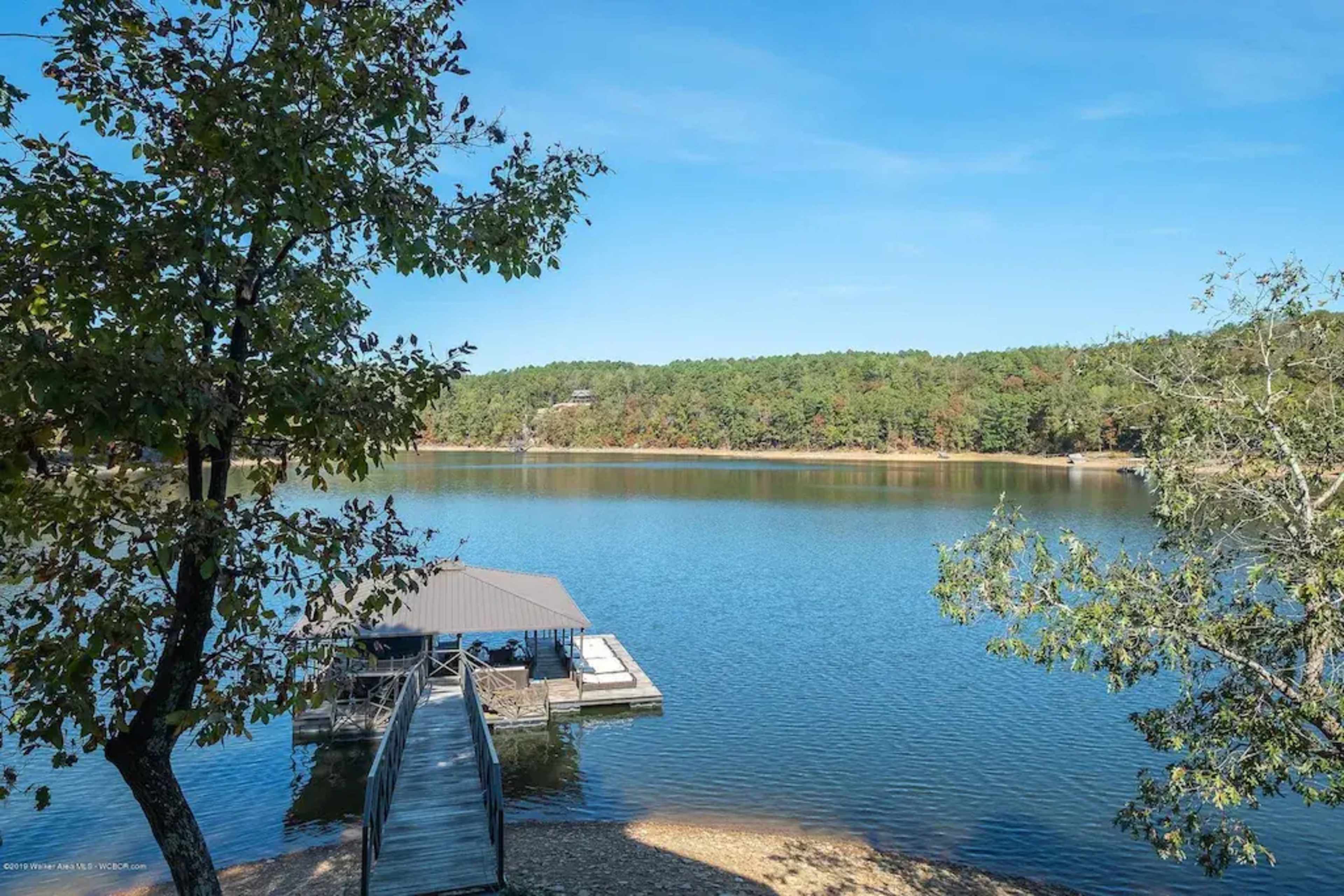 A calm lake bordered by trees, with a dock extending into the water on one side.