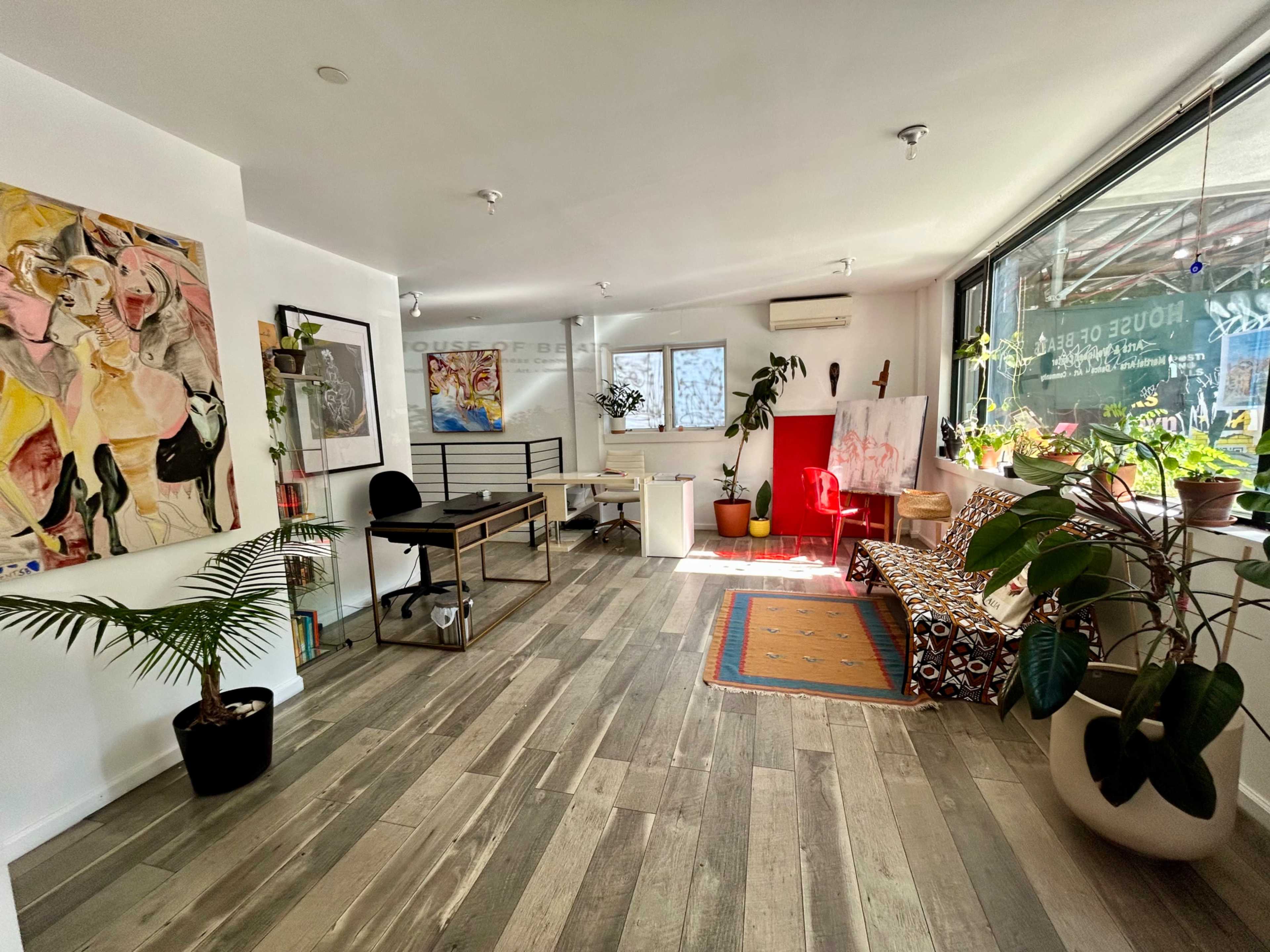 The image shows a bright, modern interior featuring a mix of artwork, plants, and contemporary furniture in a spacious room.