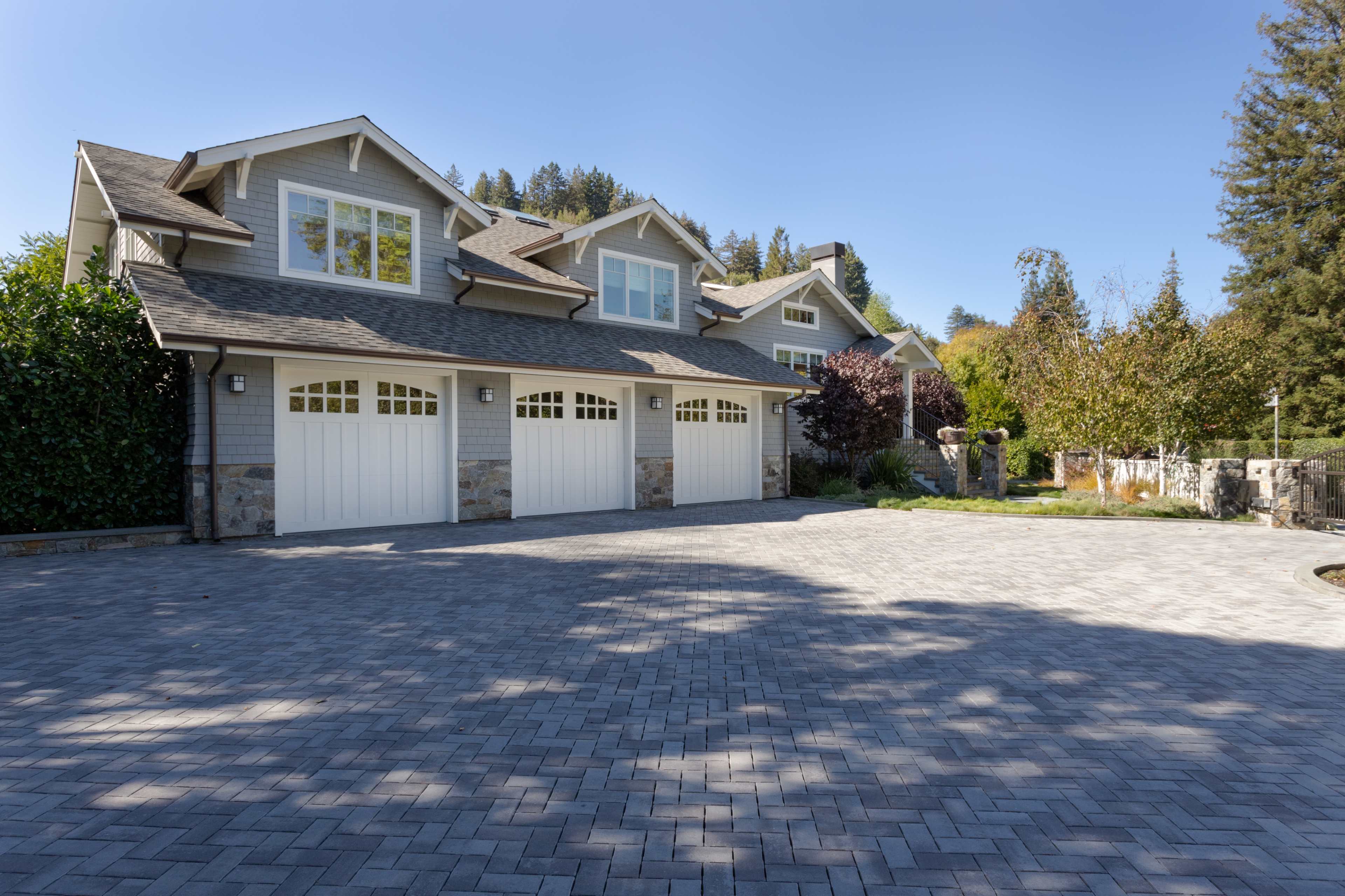 A large house with a multi-car garage and a paved driveway is surrounded by trees and landscaping.