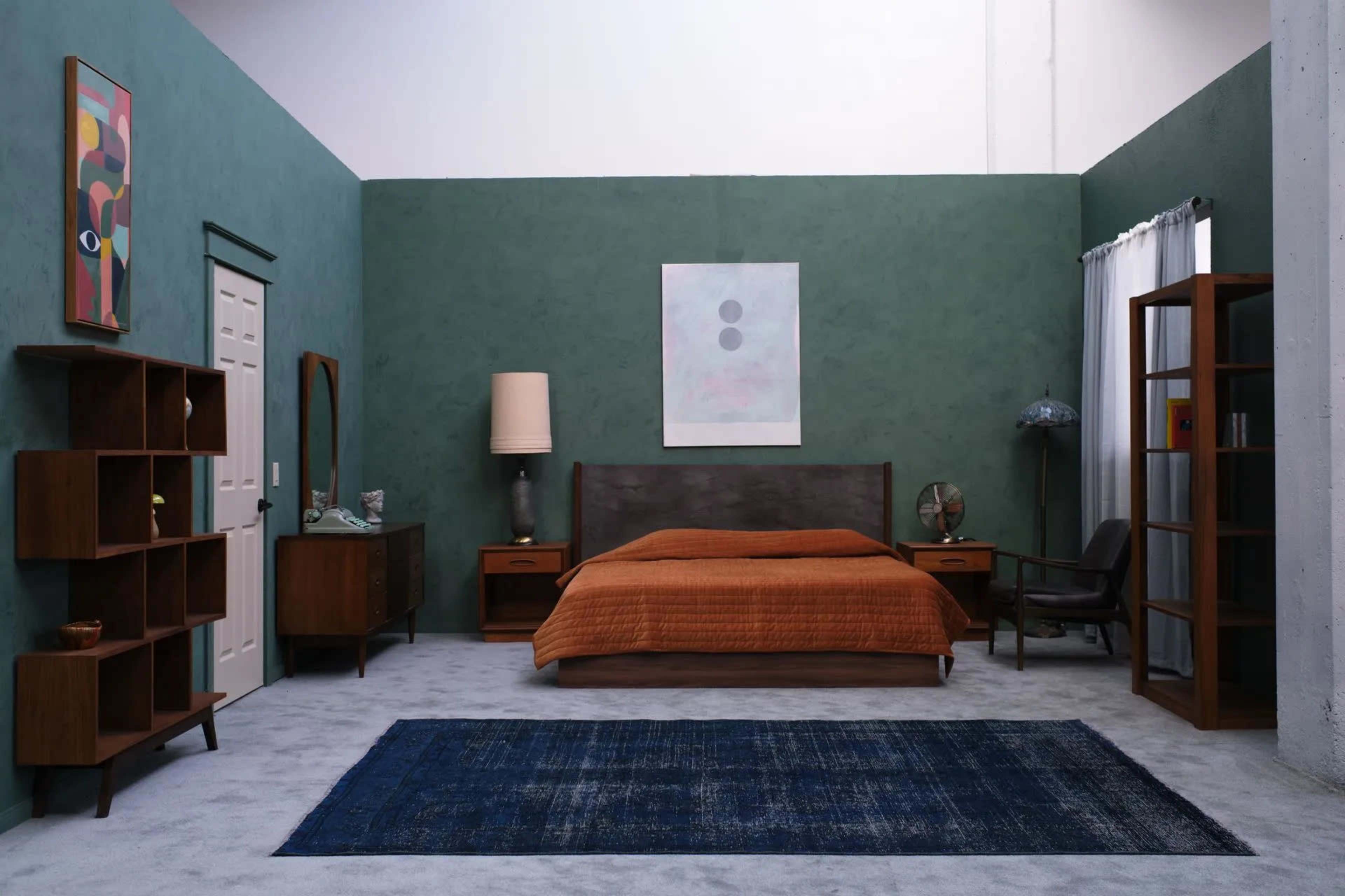 The image shows a modern bedroom featuring a brown bedspread, wooden furniture, an area rug, and green walls.