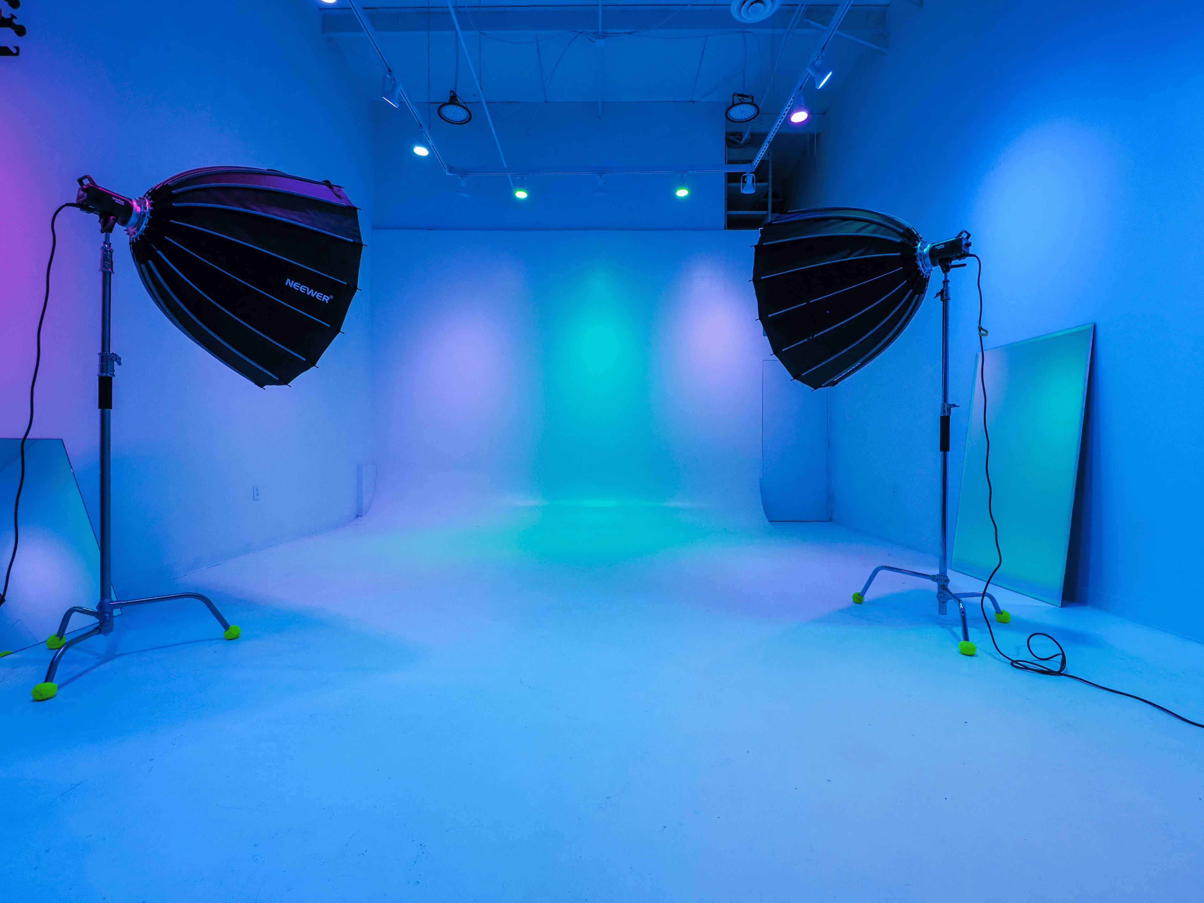 A photography studio with two large softbox lights positioned on either side, illuminating a blank backdrop in a blue and purple hue.