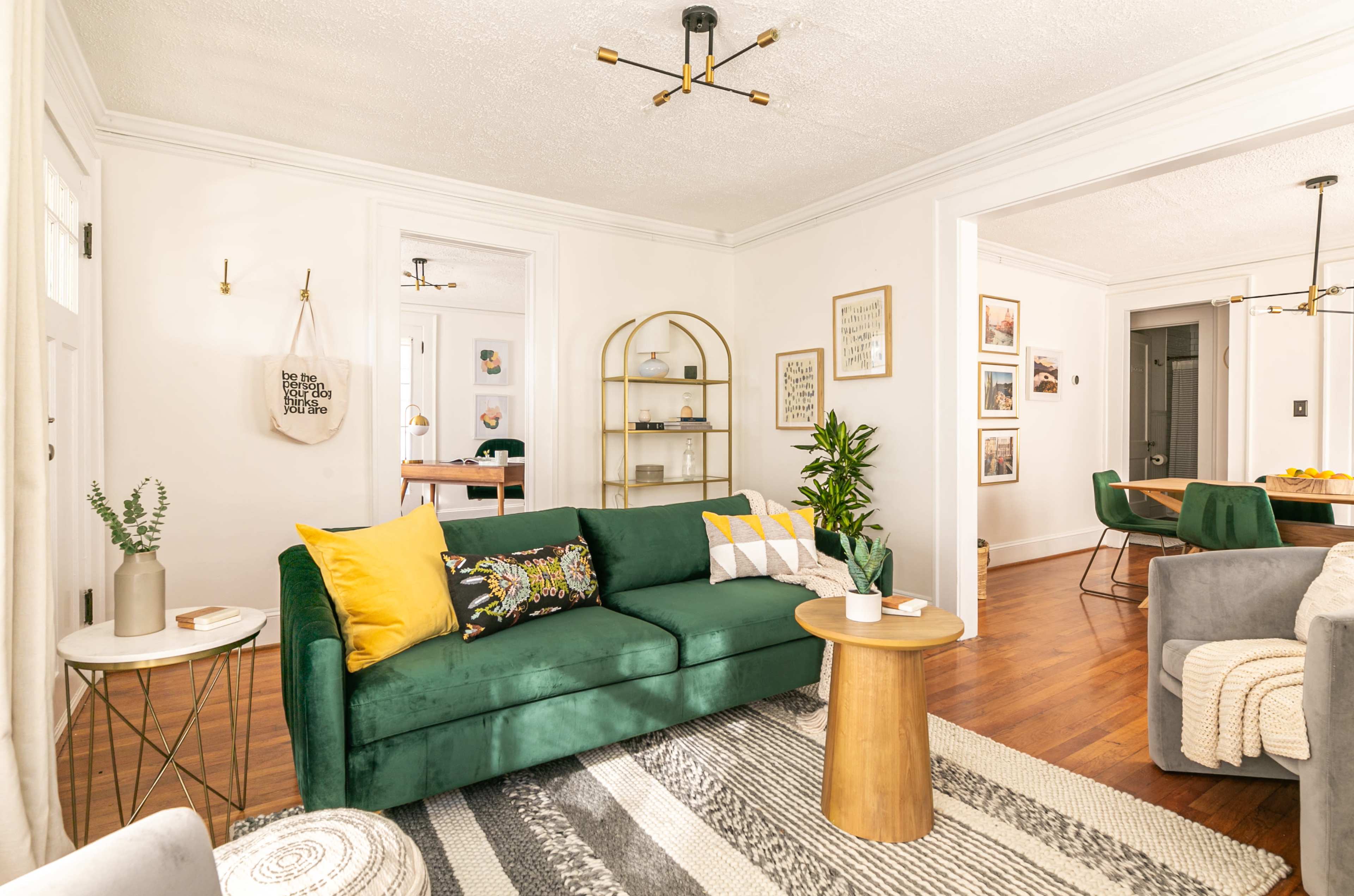 The living room features a green couch with yellow and patterned pillows, a wooden coffee table, and a decorative shelf against a light-colored wall.