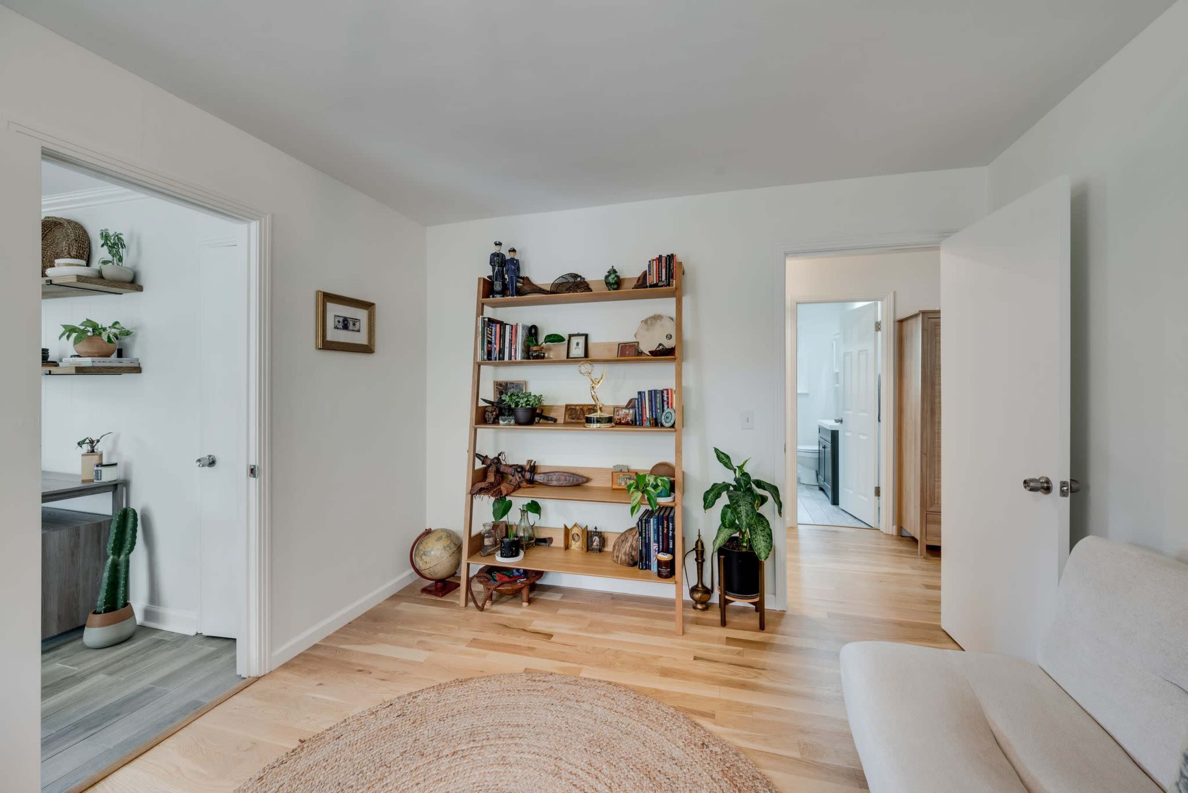 A bright room featuring a bookshelf filled with books and decor, a small globe, and plants, with doorways leading to neighboring spaces.