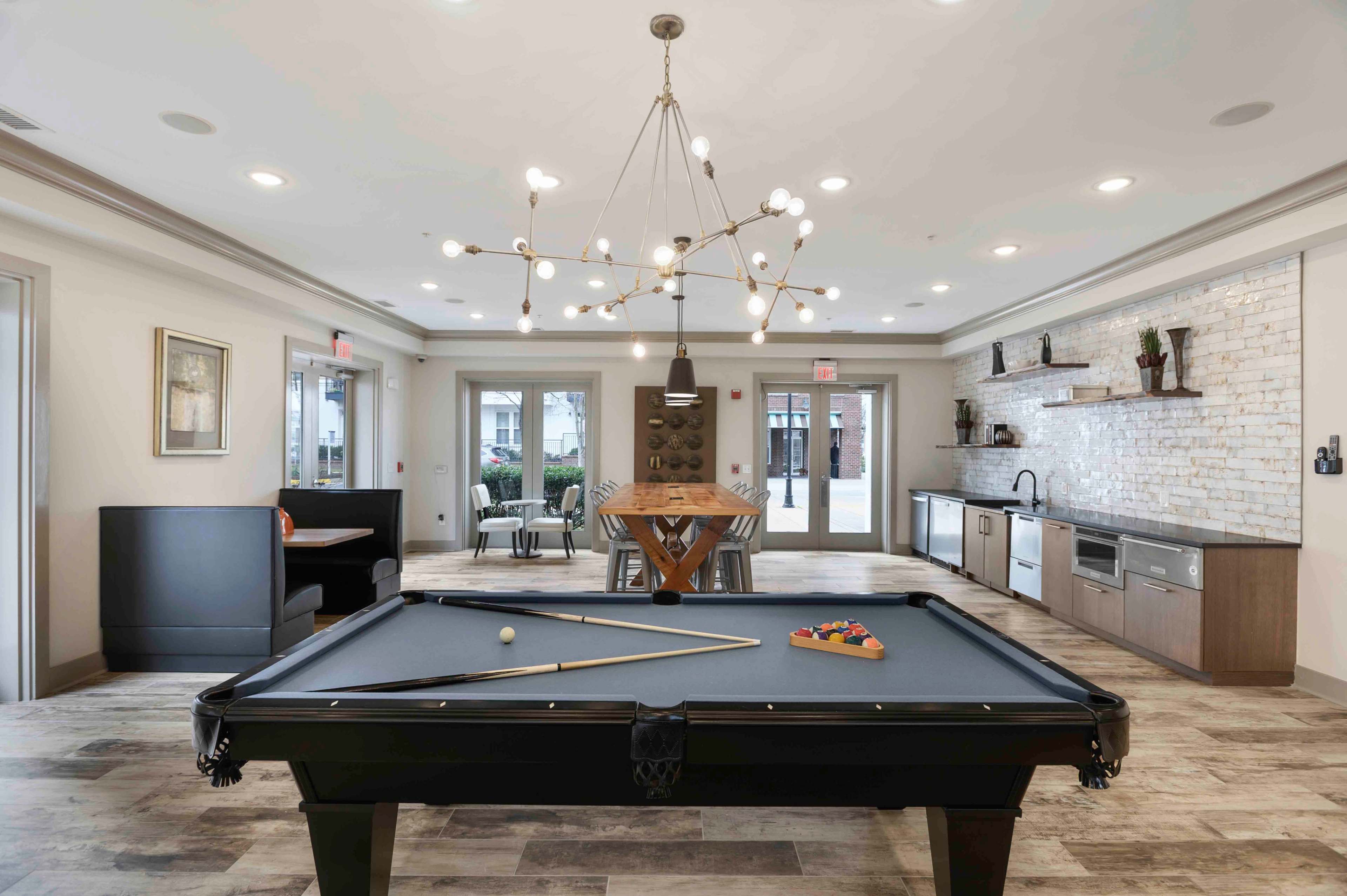 A modern recreation room featuring a pool table, dining table, and kitchen area with a decorative wall.