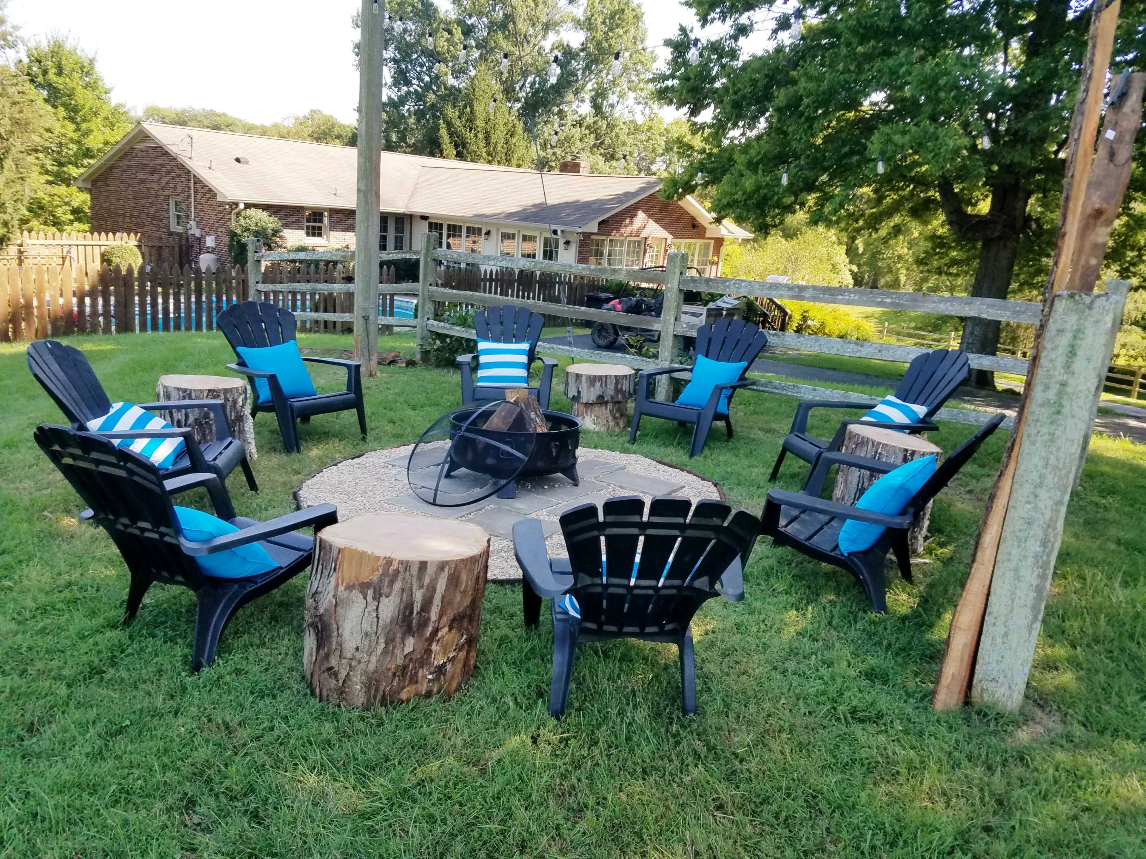 A circular seating area made of black chairs around a fire pit, surrounded by grassy terrain and rustic wooden elements.