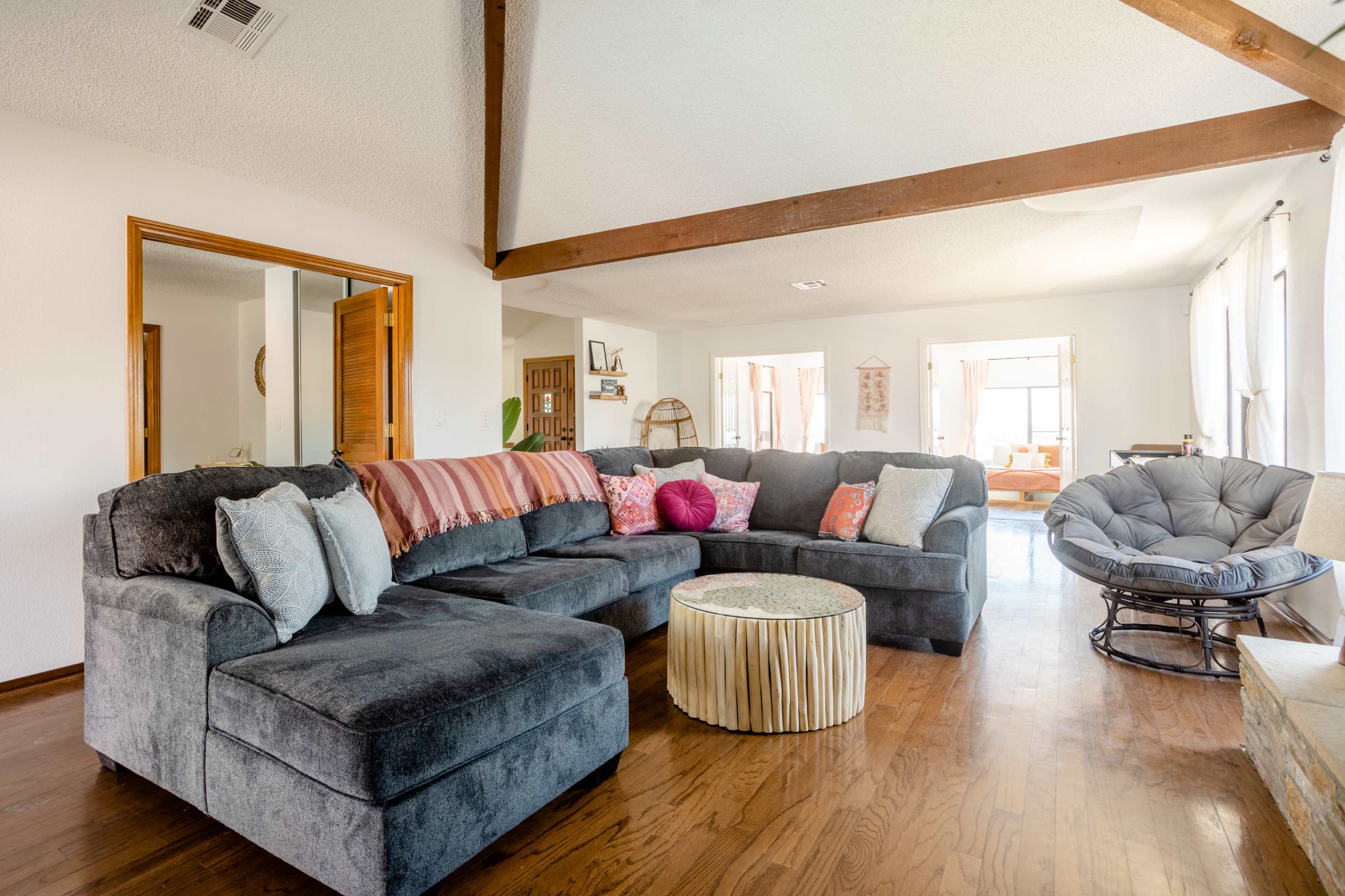 A spacious living room with a large gray sectional sofa, a round coffee table, and natural light coming through multiple windows.