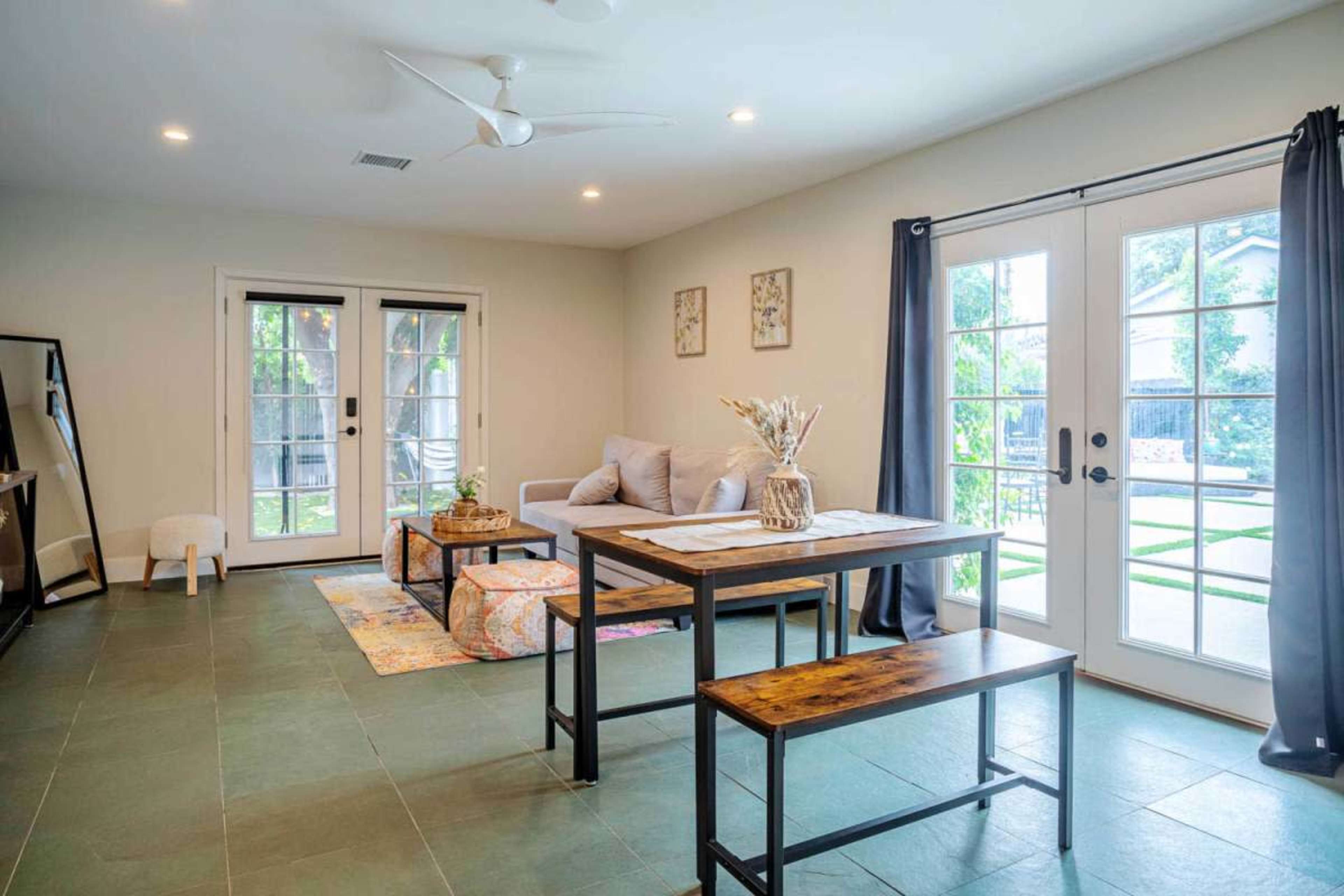 A modern living space with a dining table, a sofa, and a pair of French doors opening to an outdoor area.
