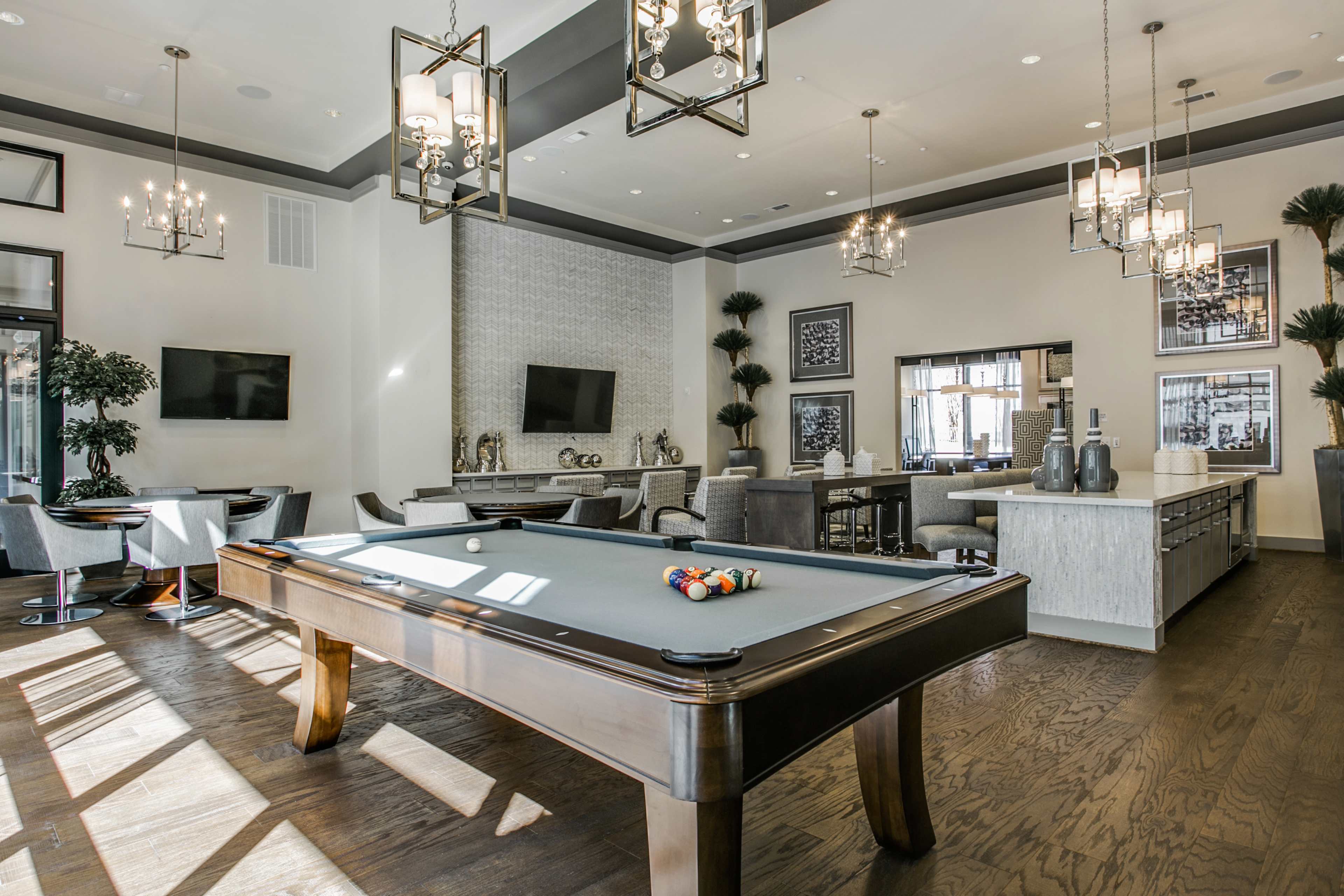 A modern game room featuring a pool table, stylish lighting fixtures, and a mix of seating areas with decorative plants.