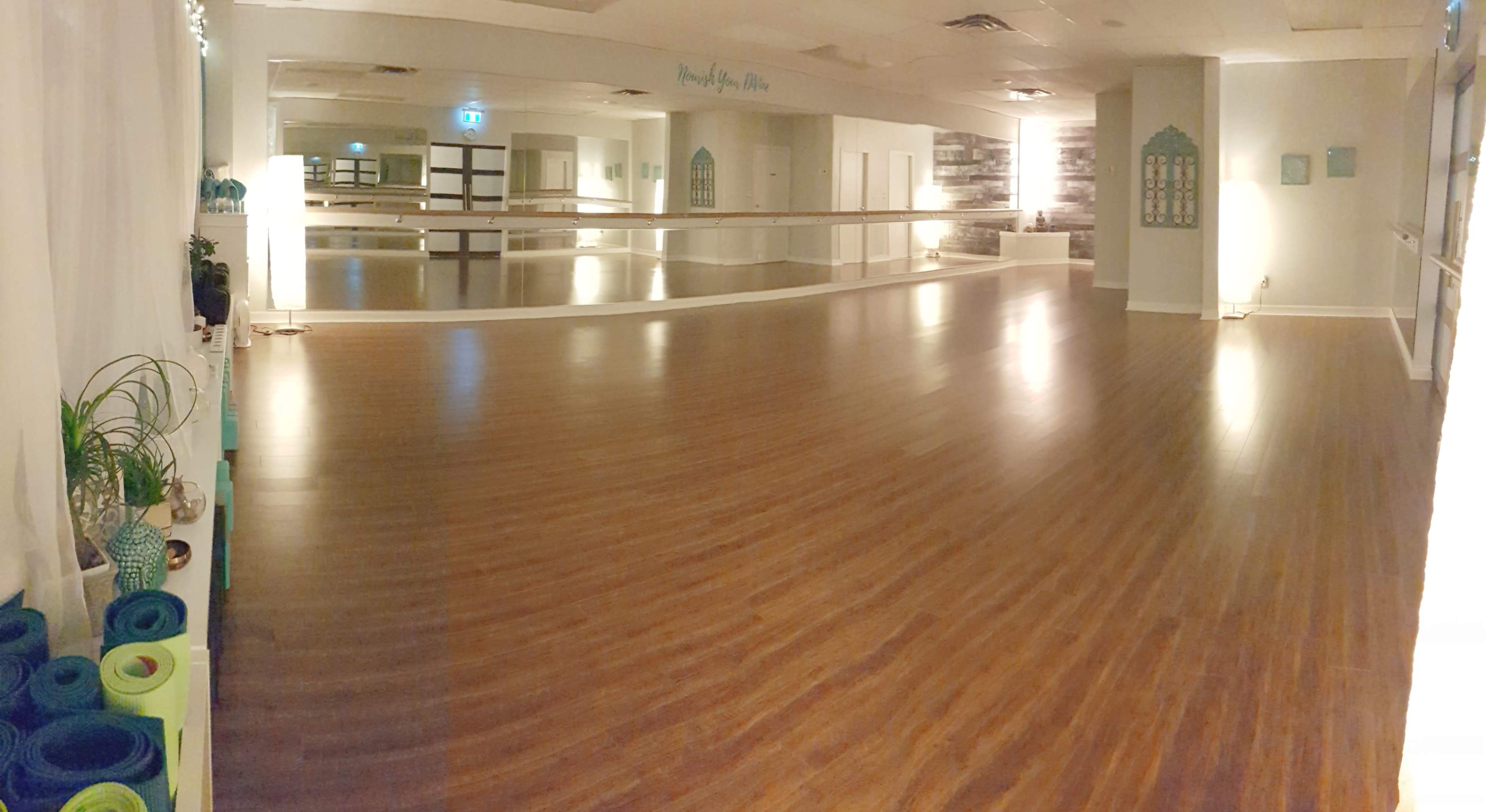 A spacious dance studio with wooden flooring, large mirrors on the walls, and various fitness mats arranged neatly along one side.