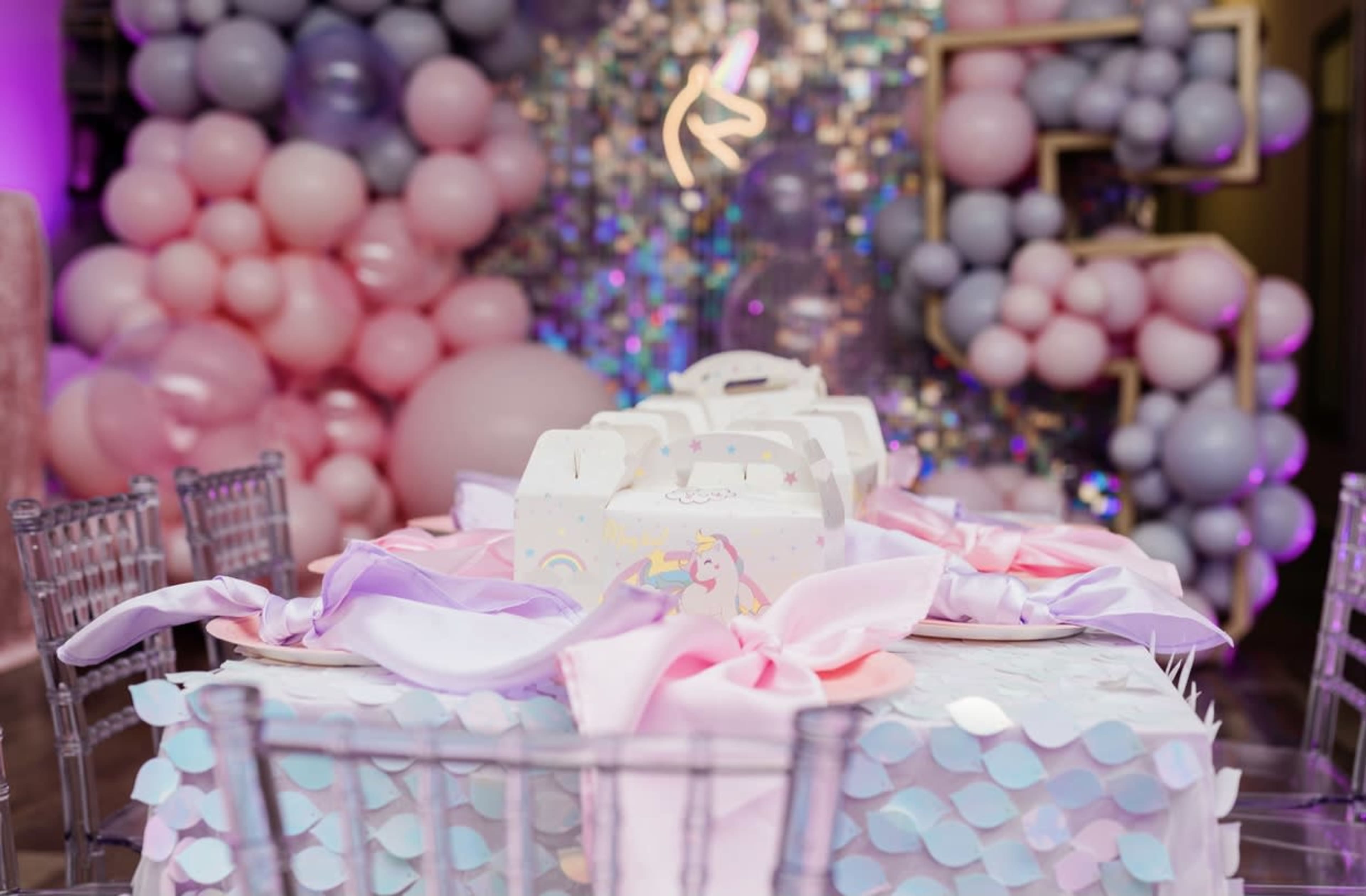A decorated table for a celebration, featuring a pastel balloon backdrop, gift boxes, and colored table settings.
