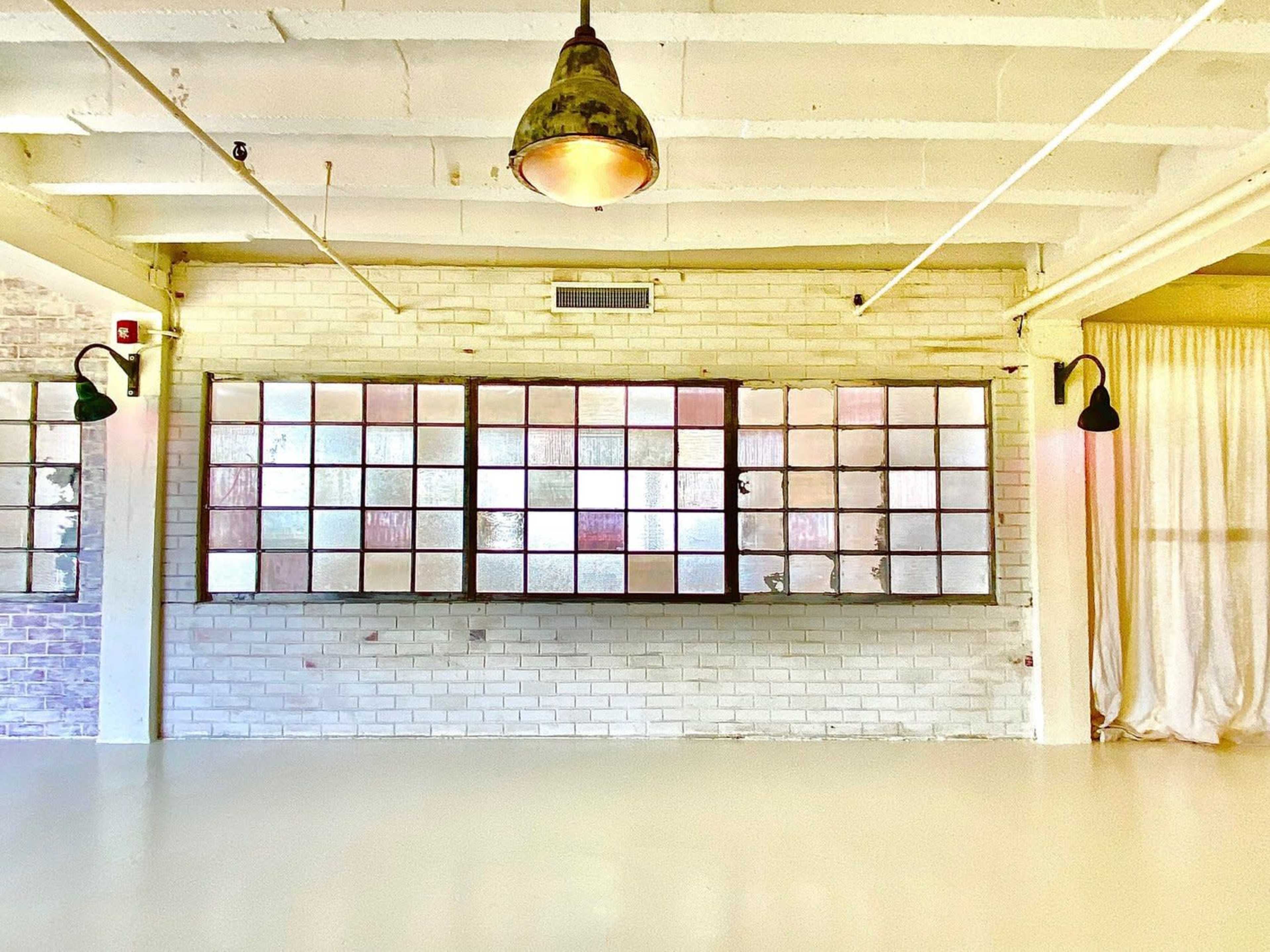 A spacious interior with a white-brick wall featuring a large grid of glass panels and a pendant light hanging from the ceiling.