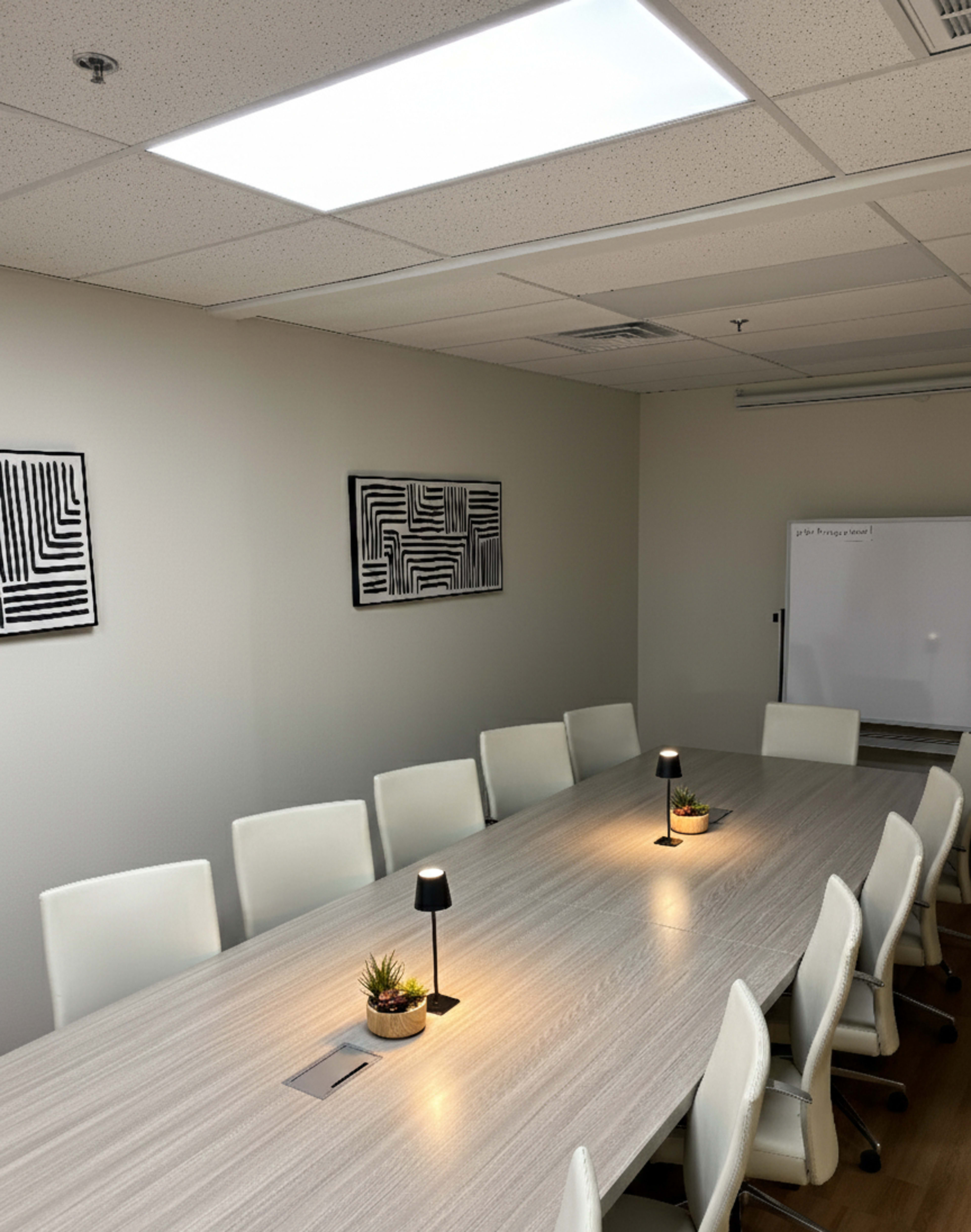 The image shows a modern conference room with a long wooden table, white chairs, and two small lamps on the table.