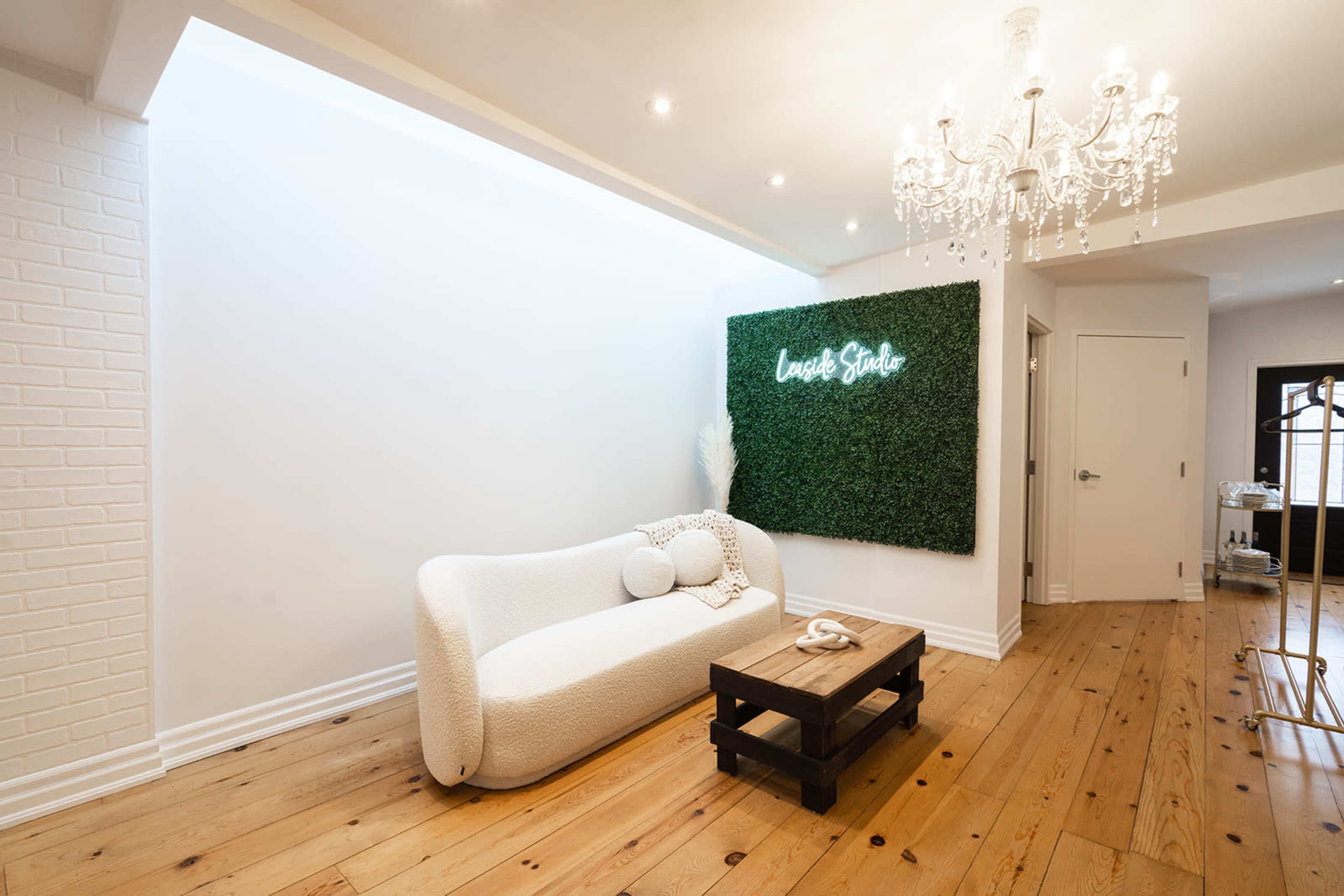 A bright and modern living space featuring a white curved couch, a wooden coffee table, and a wall adorned with greenery and a neon sign.