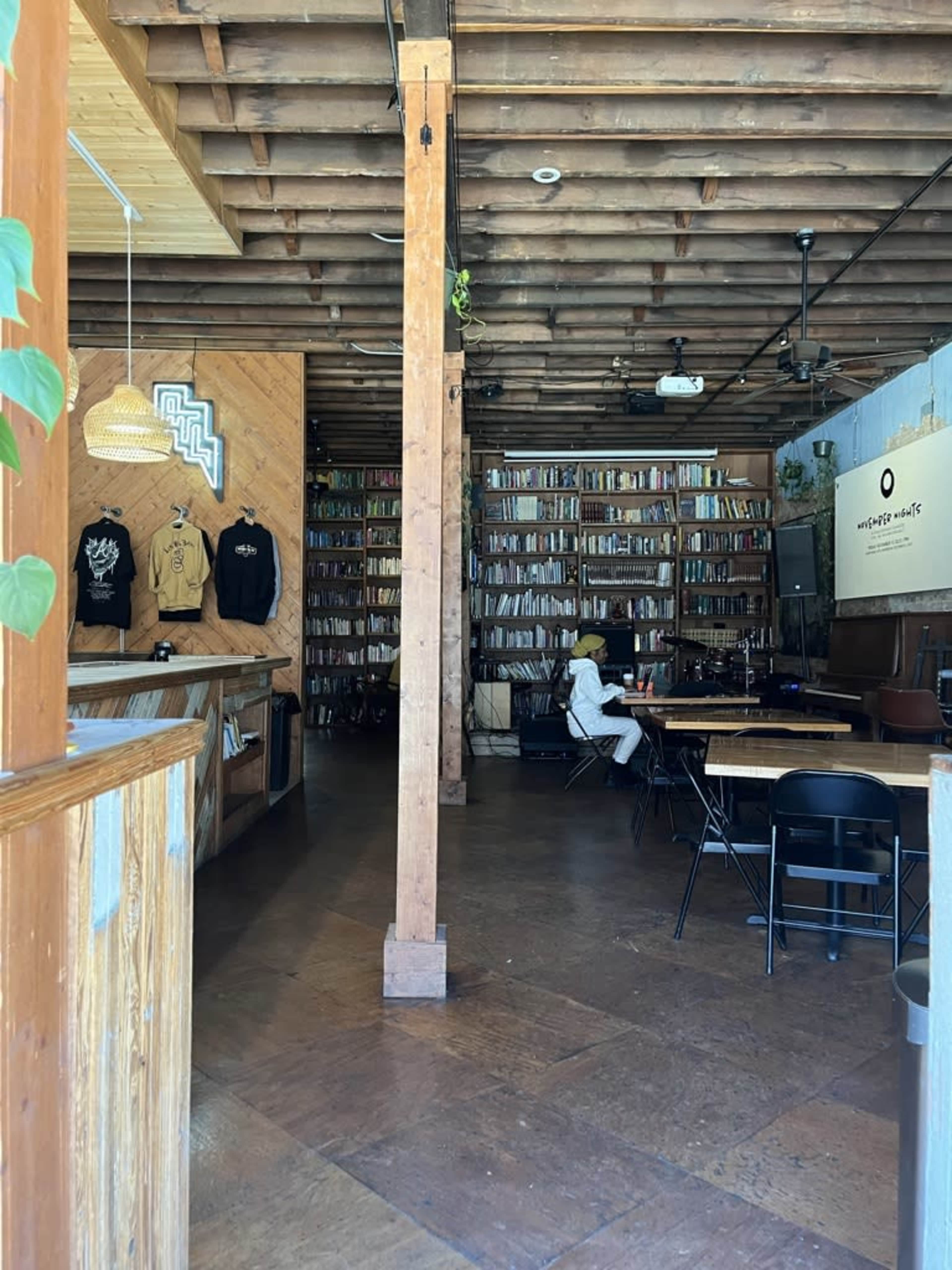 The interior of a café features wooden beams and a wall lined with shelves full of books.
