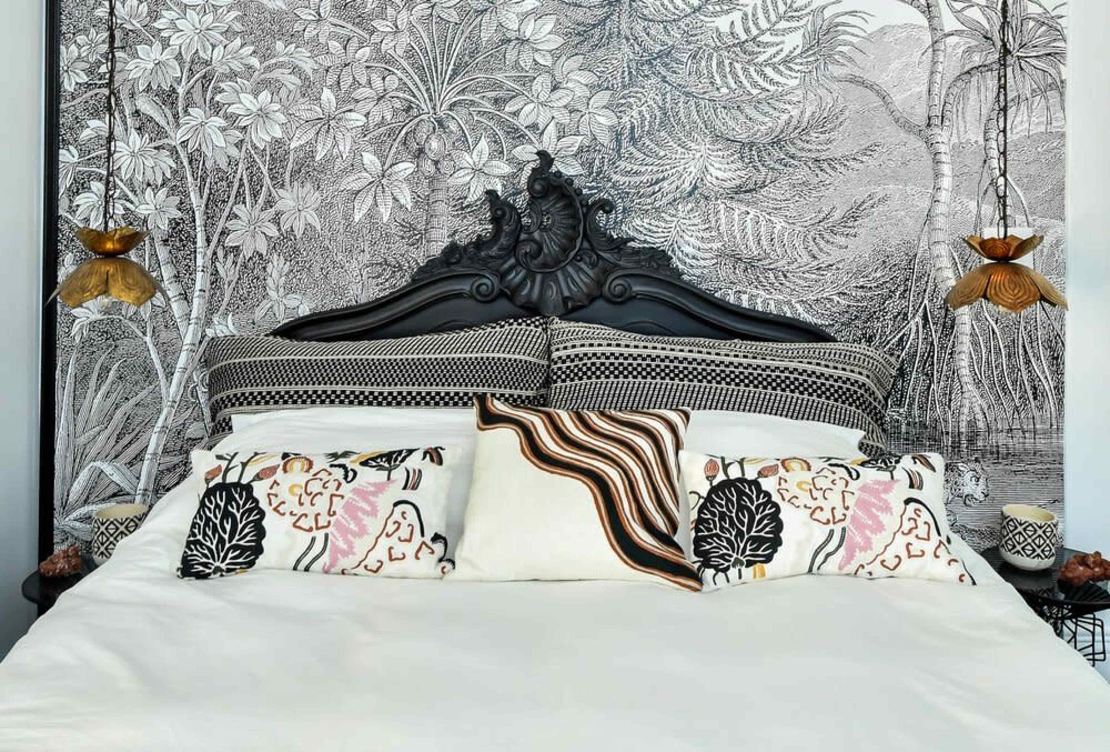 The image features a bed with a black ornate headboard and decorative pillows against a detailed floral wallpaper backdrop.