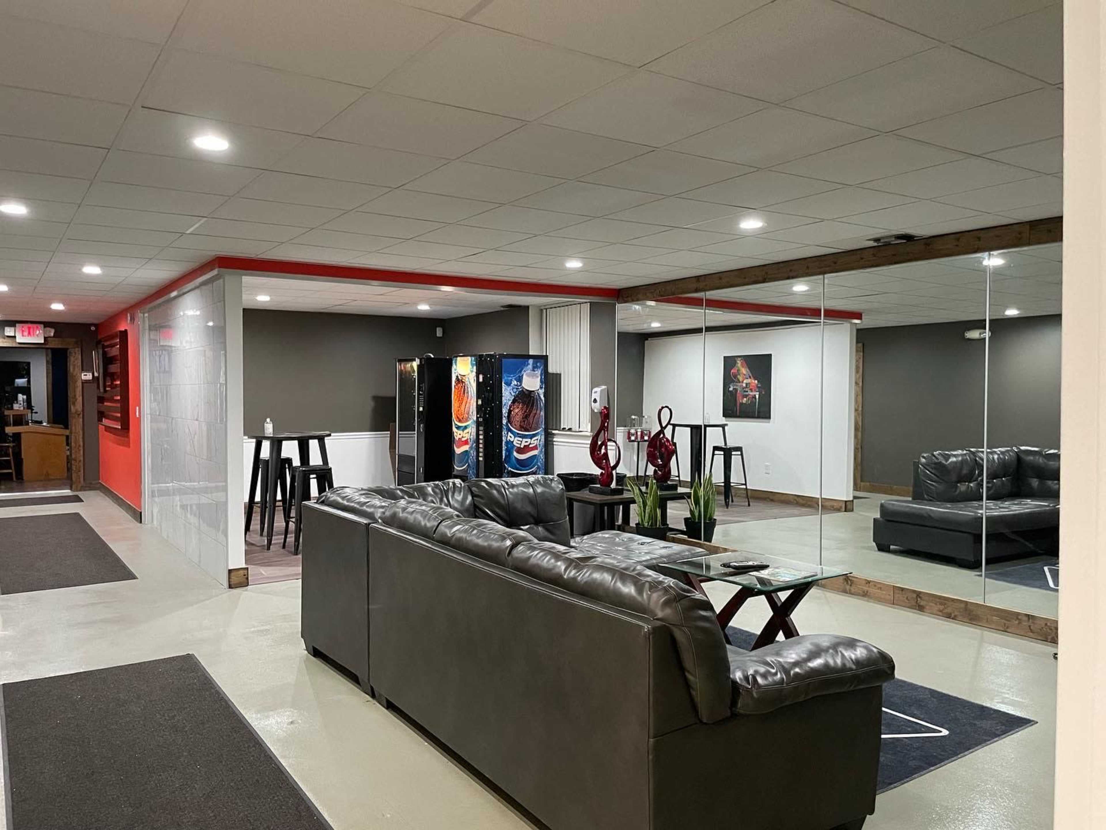 A lounge area with a sleek couch, a coffee table, vending machines, and a mirrored wall in a well-lit setting.