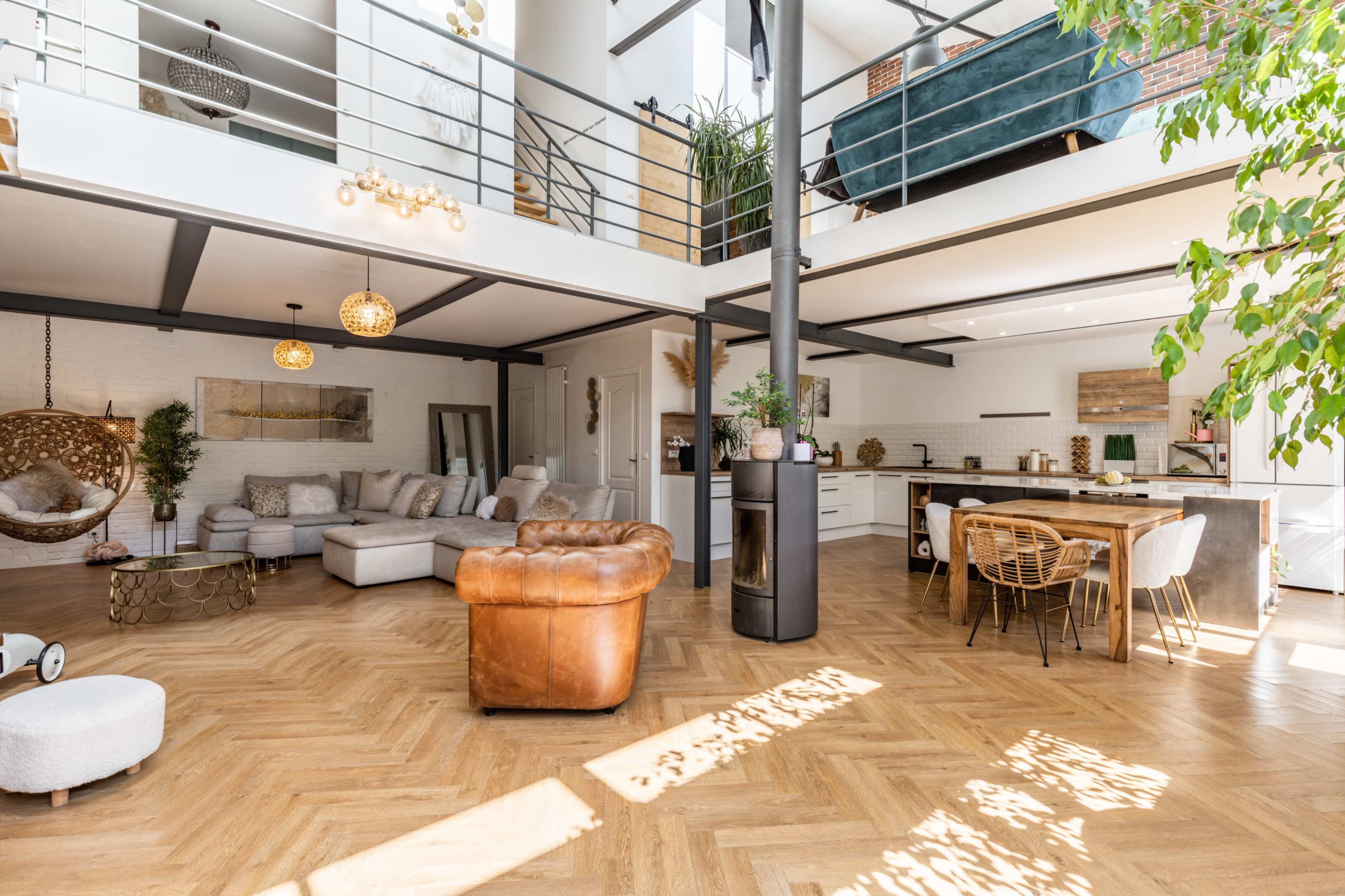 A spacious, modern living area with a kitchen, dining table, and a brown leather seating arrangement, all featuring wooden flooring and ample natural light.