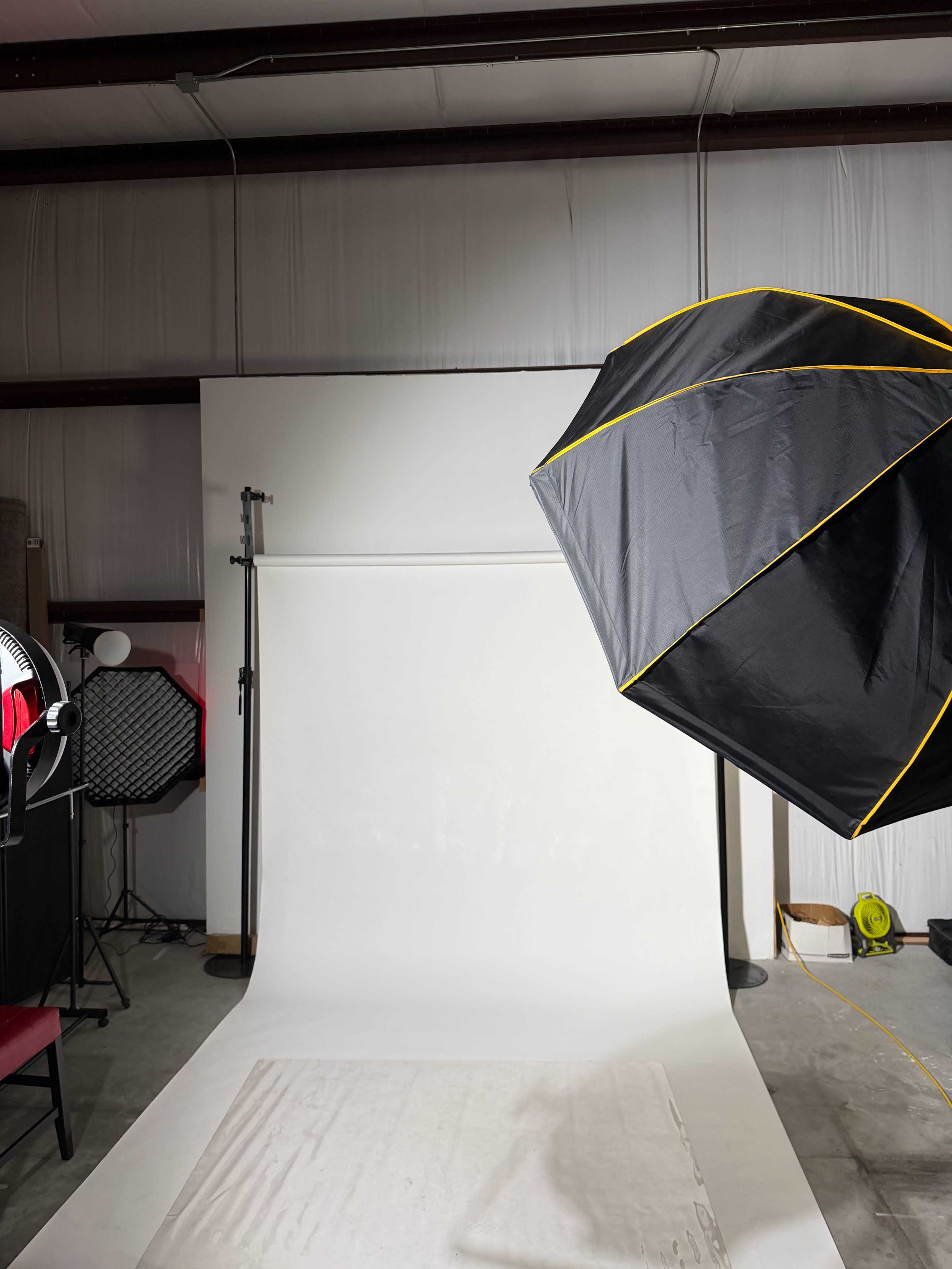 The image shows a photography studio setup featuring a large softbox light and a plain white backdrop.