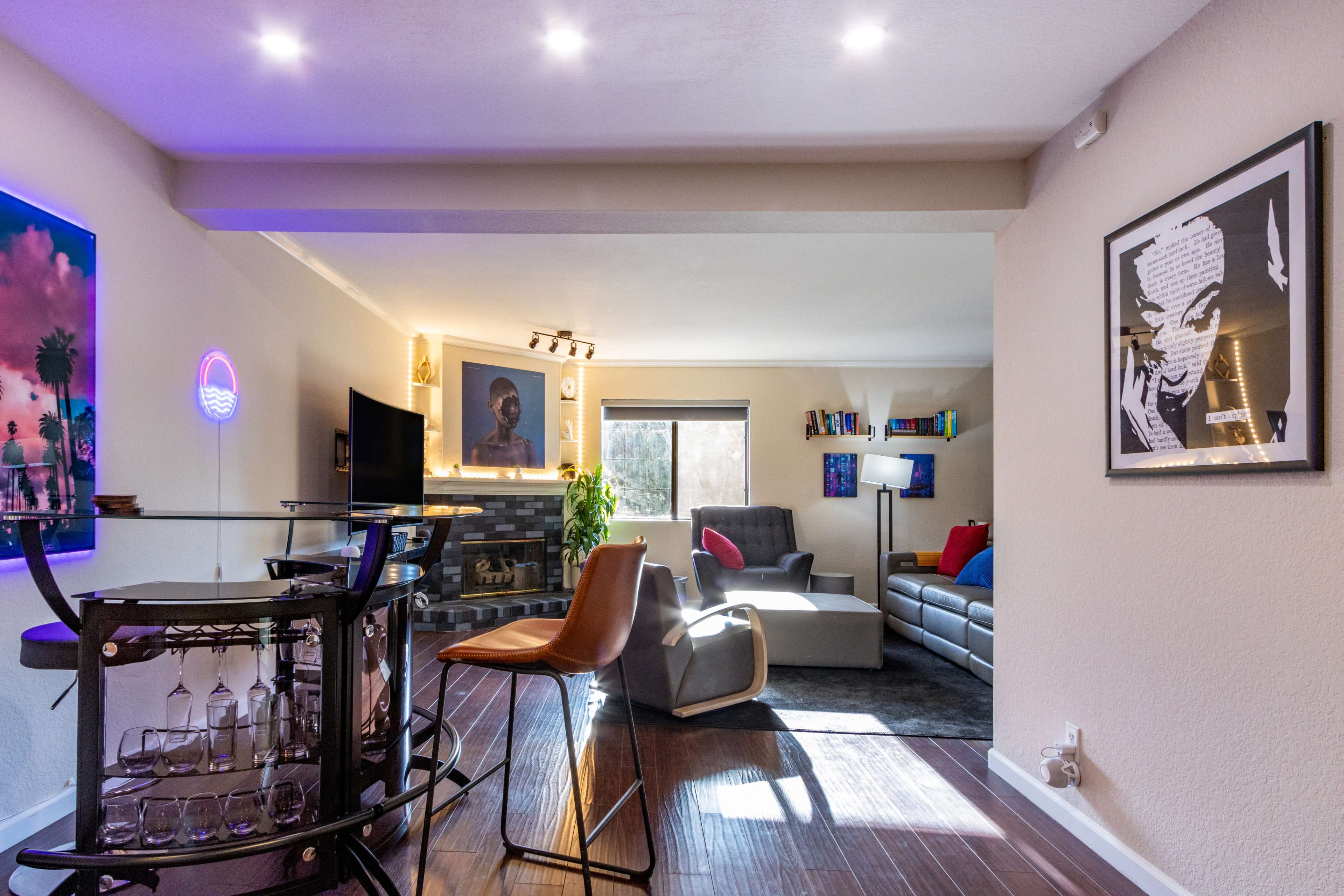 A cozy living space features a bar cart, comfortable seating, and artwork on the walls, with ample natural light coming through a window.