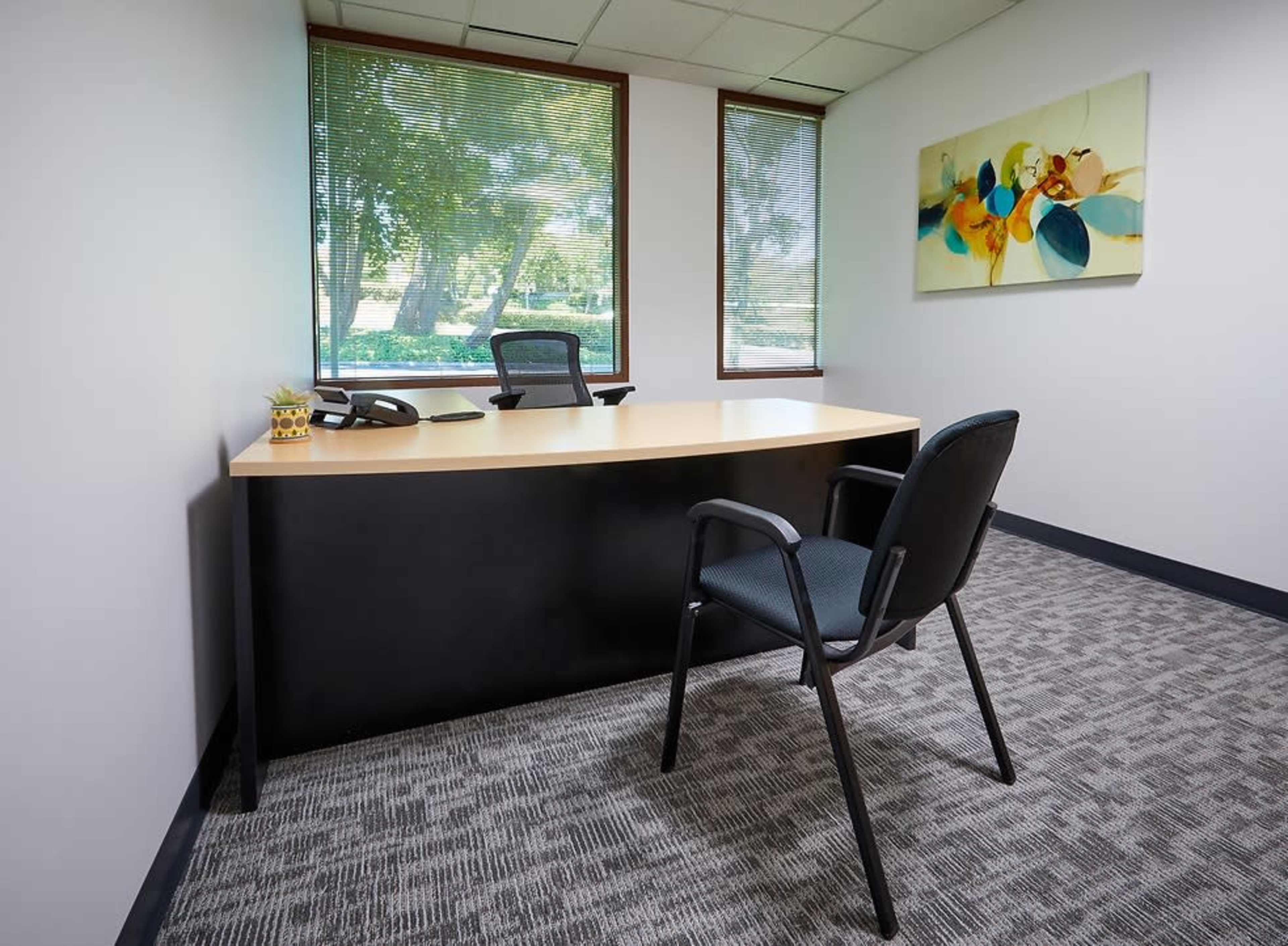 An office space featuring a desk, an ergonomic chair, a phone, and a large window with natural light.