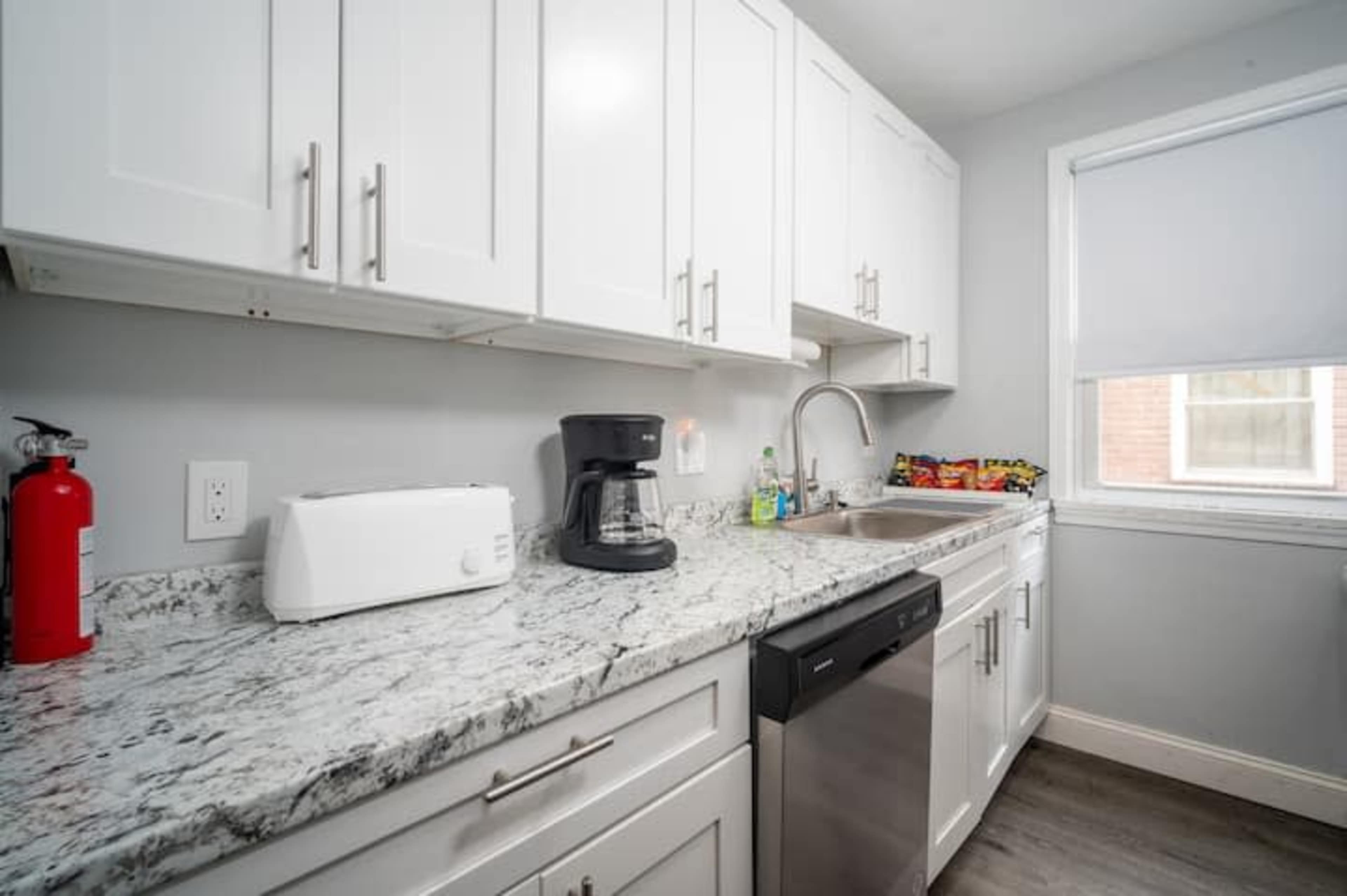 A modern kitchen with white cabinets, a stainless steel sink, a coffee maker, and a variety of food items on the counter.