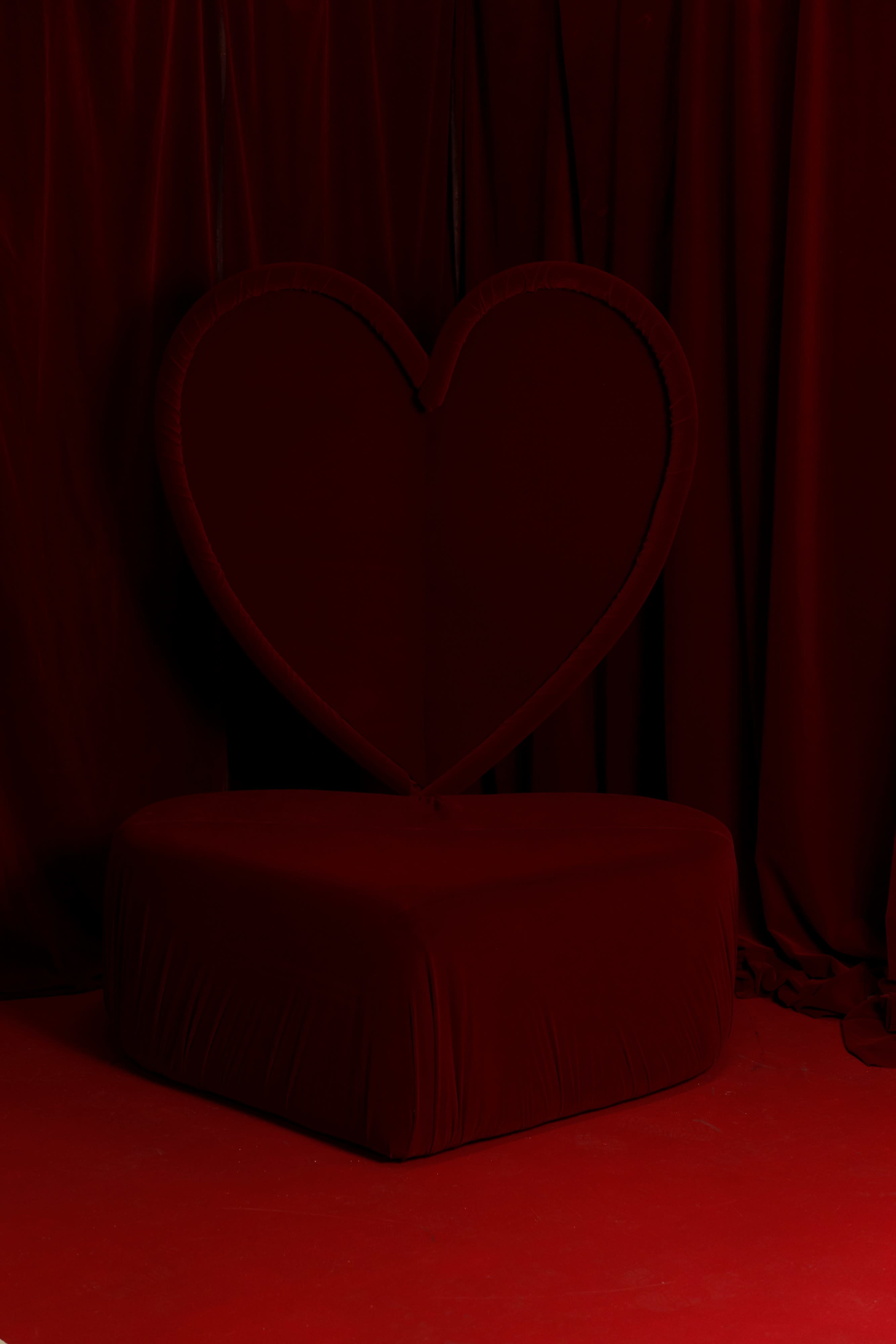 A heart-shaped chair is positioned against a red backdrop, surrounded by matching red fabric.