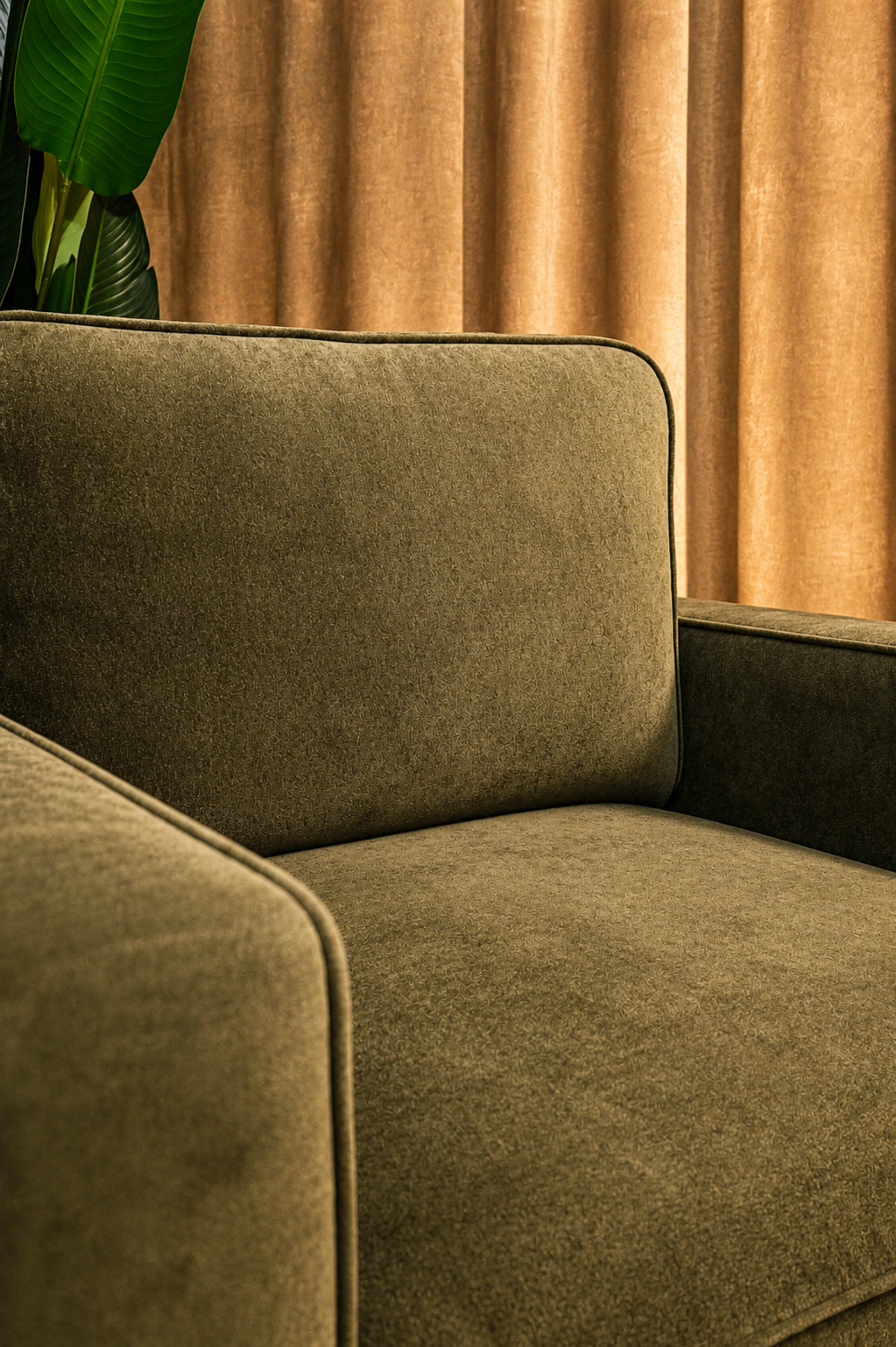 The image shows a close-up of a green sofa with a textured fabric, set against a backdrop of warm, golden curtains.