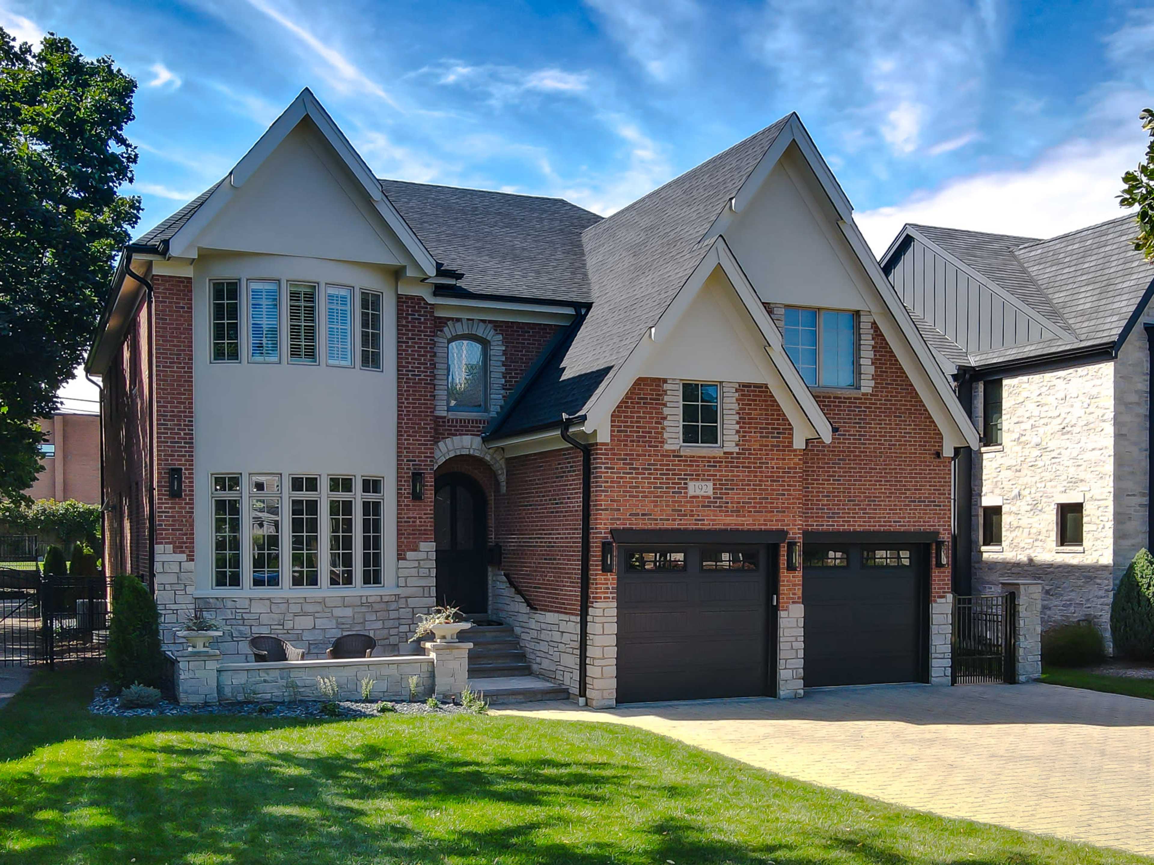The image shows a modern two-story brick house with a stone foundation, featuring a driveway and well-maintained landscaping.