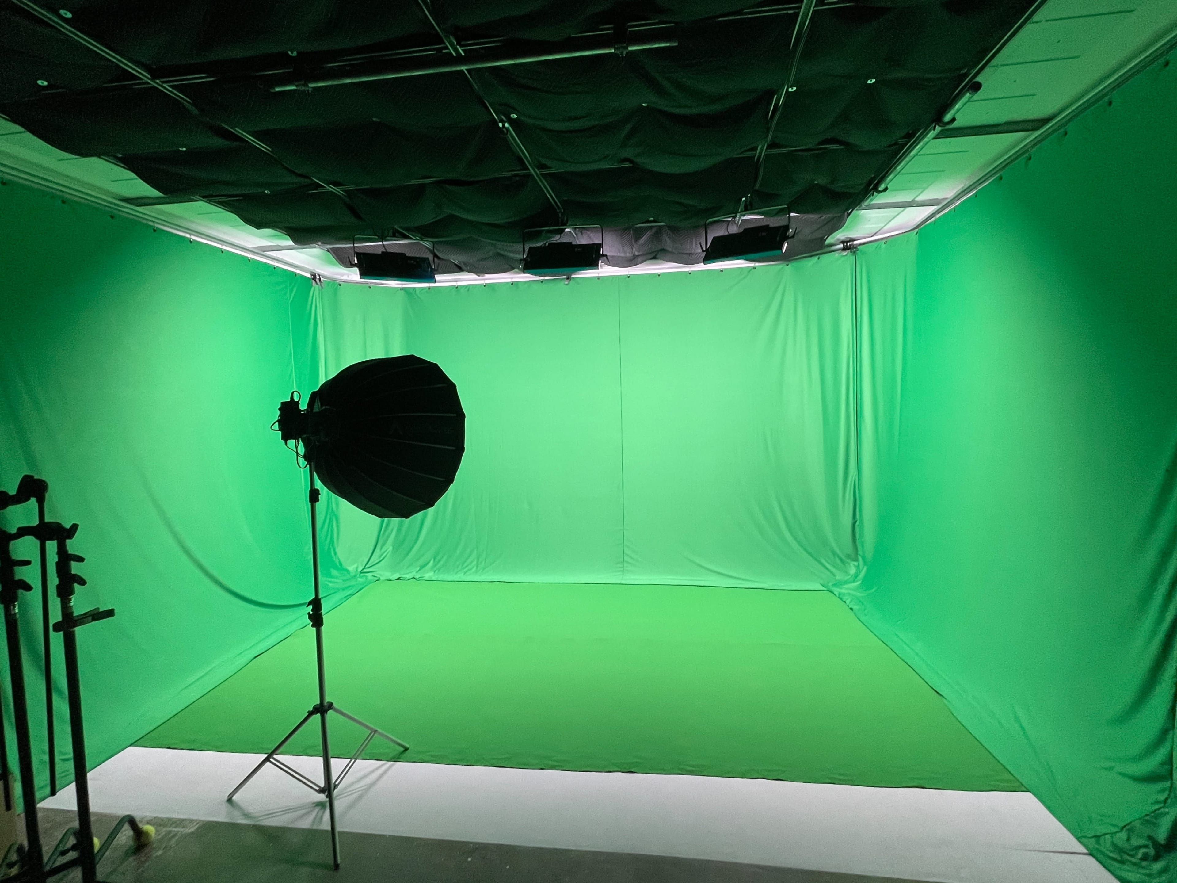 The image shows a green screen studio with uniform green fabric draping the walls and floor, along with a large softbox light on a stand.
