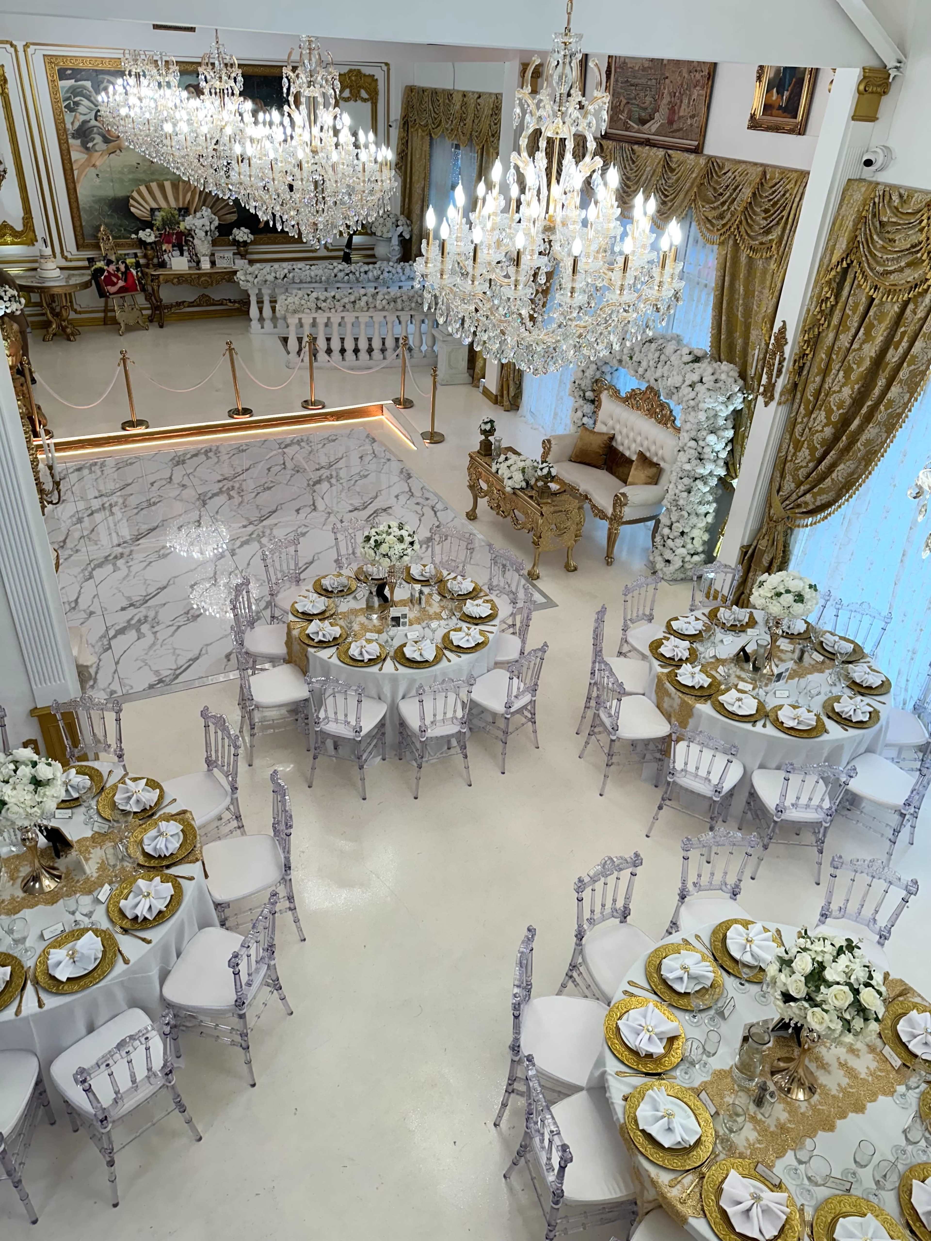 The image shows an elegantly decorated banquet hall with round tables set for dining, featuring floral centerpieces and crystal chandeliers above.