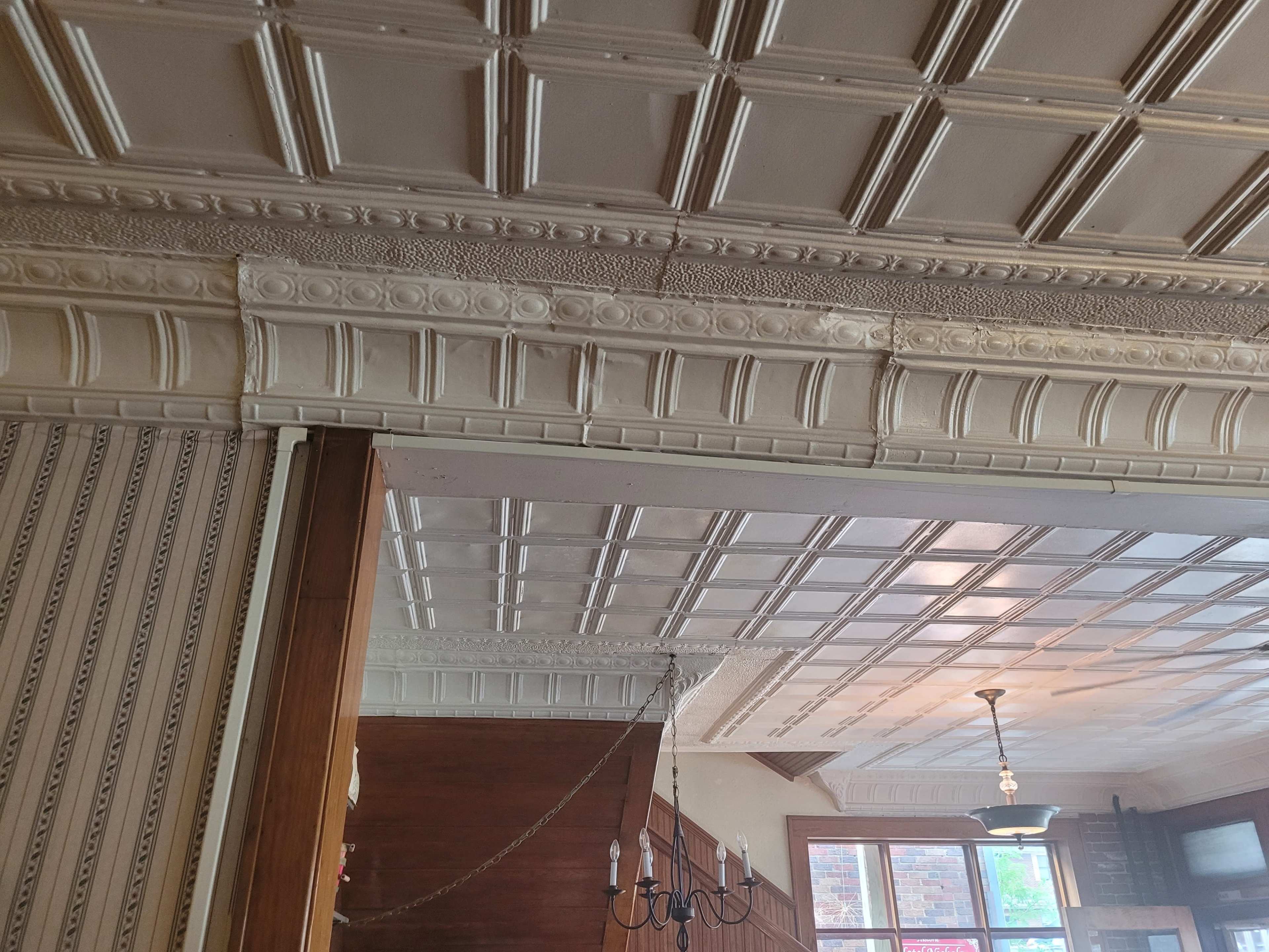 A room with decorative plaster moldings on the ceiling and walls, featuring a chandelier.
