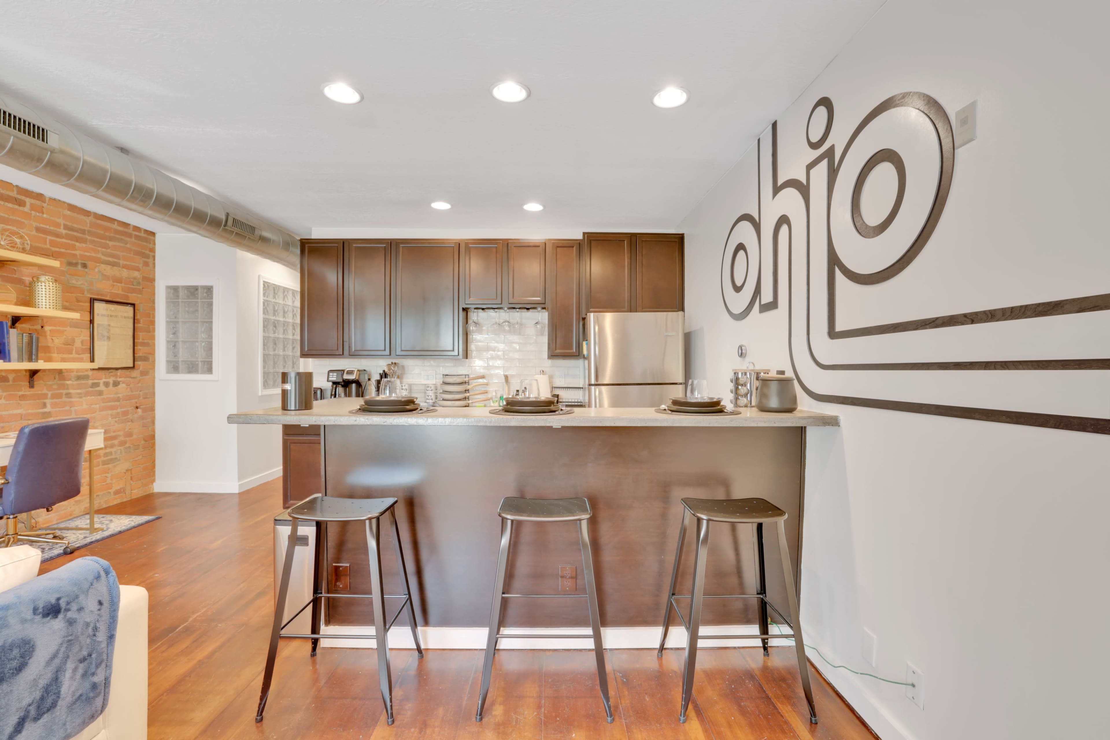 A modern kitchen area with a dark wood countertop, three black bar stools, and a decorative wall featuring the word "ohio."