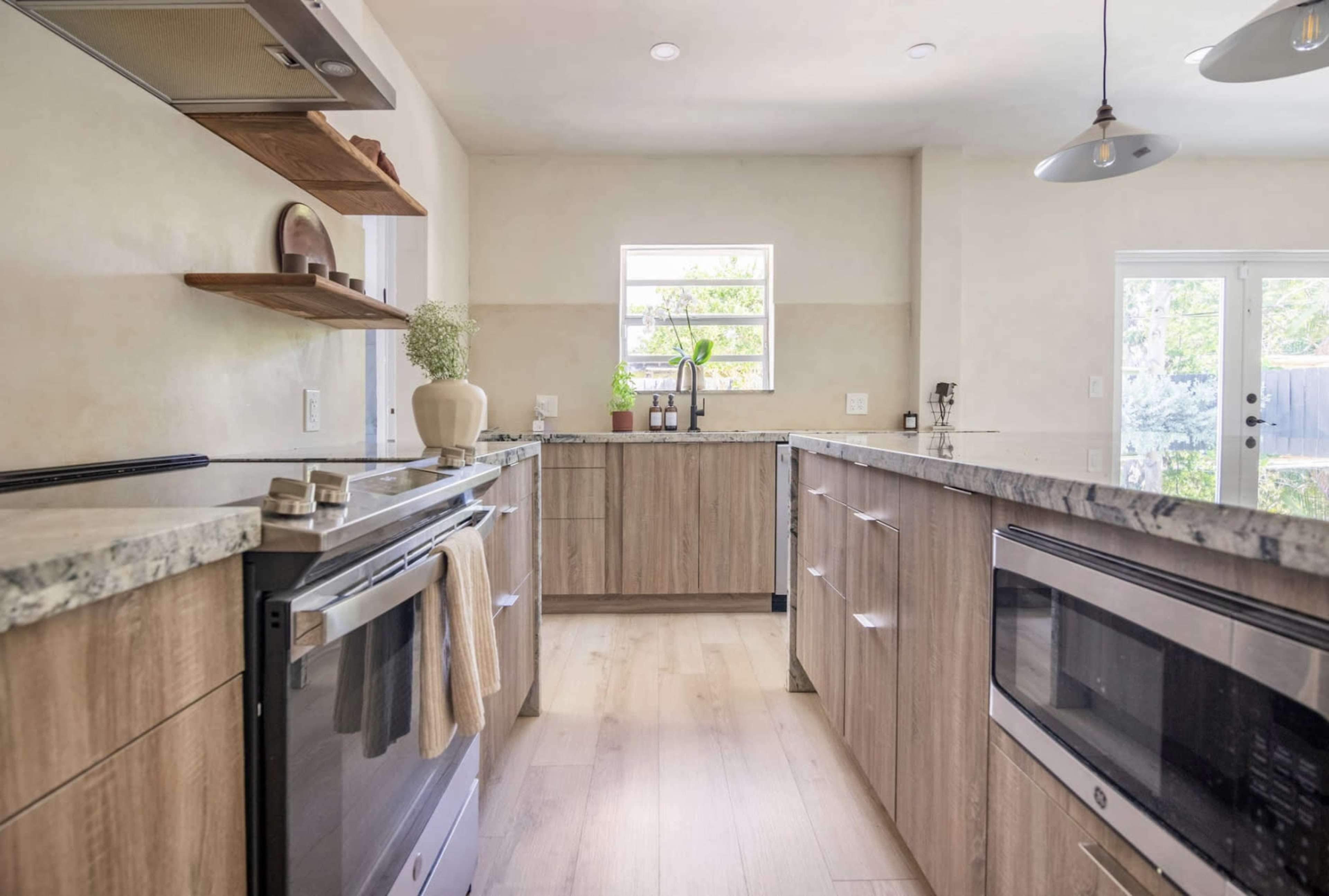 A modern kitchen features wooden cabinetry, a granite countertop, and appliances, with a window and door providing natural light.