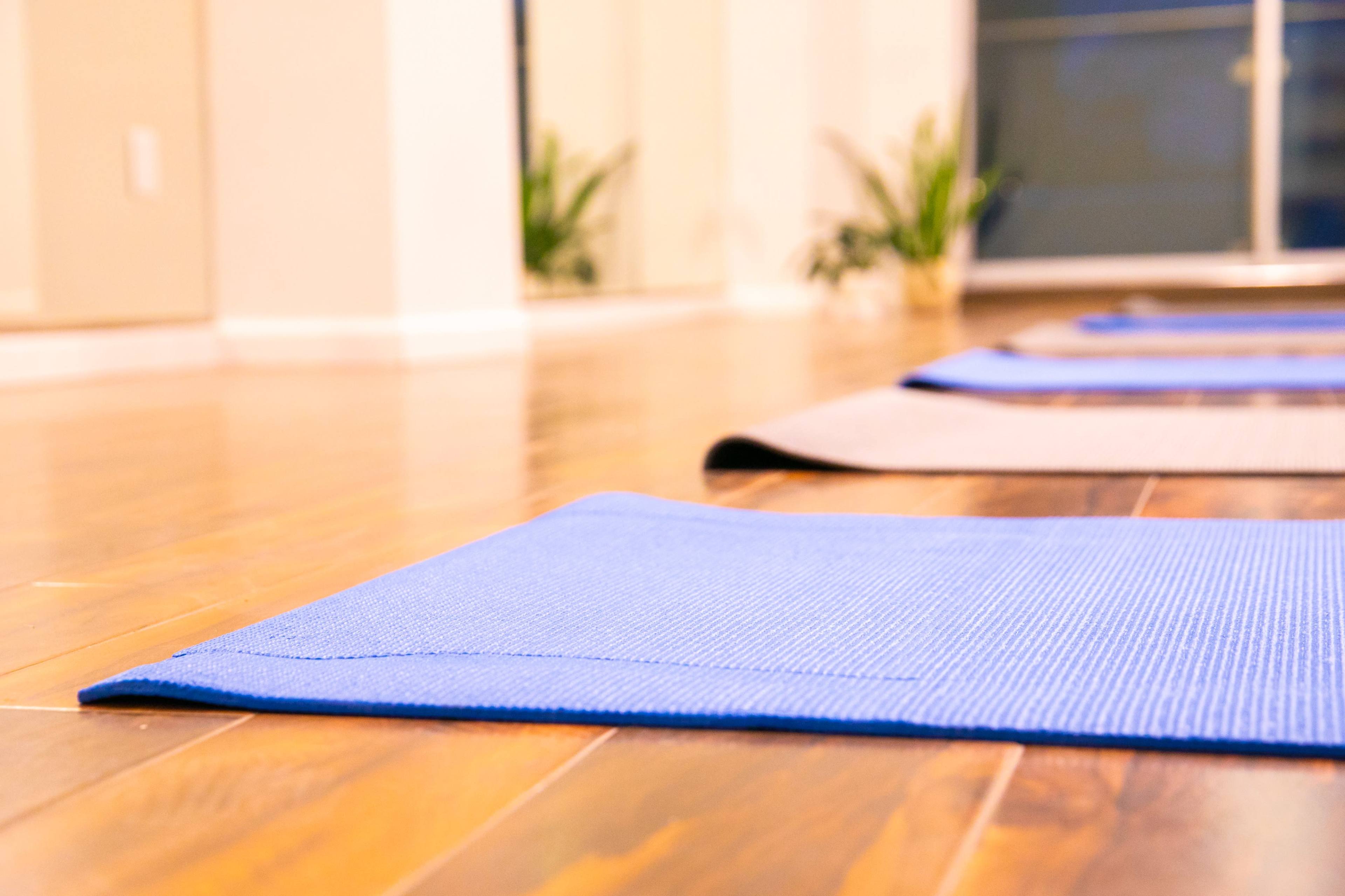 Blue and gray yoga mats arranged on a polished wooden floor in a room with large mirrors and plants in the background.