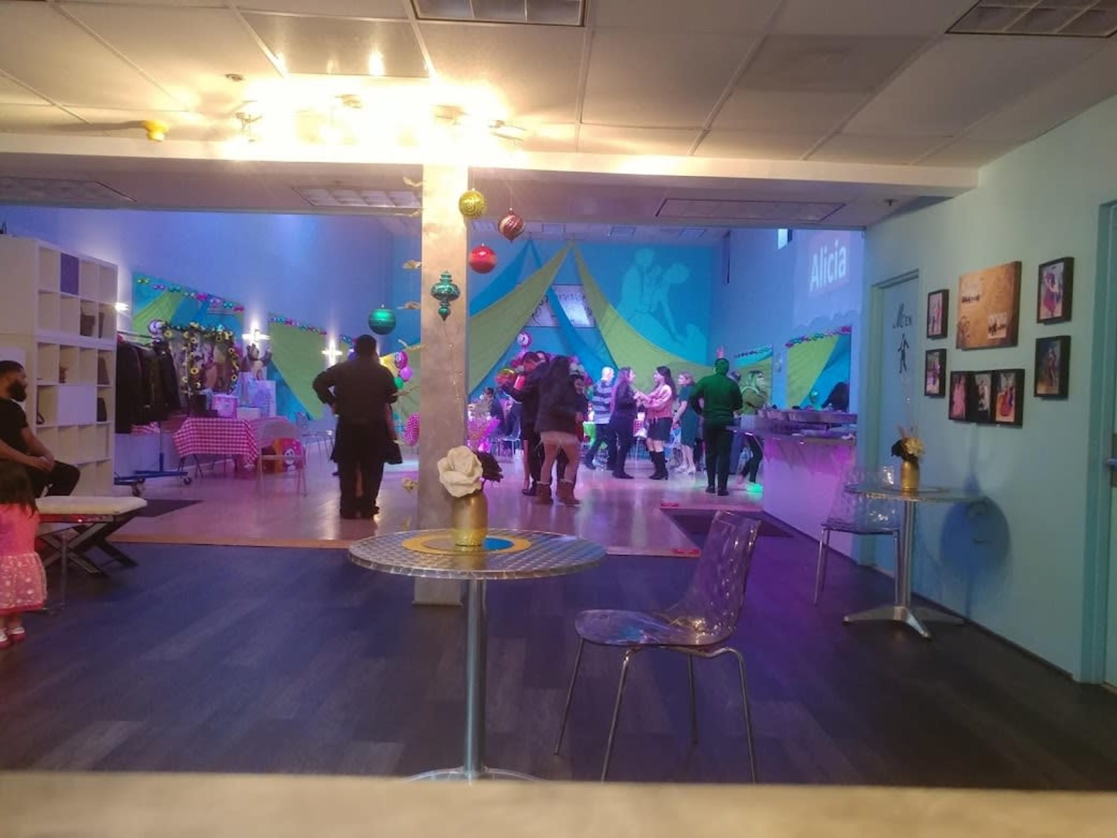A group of people dance on a brightly lit floor in a decorated indoor venue.