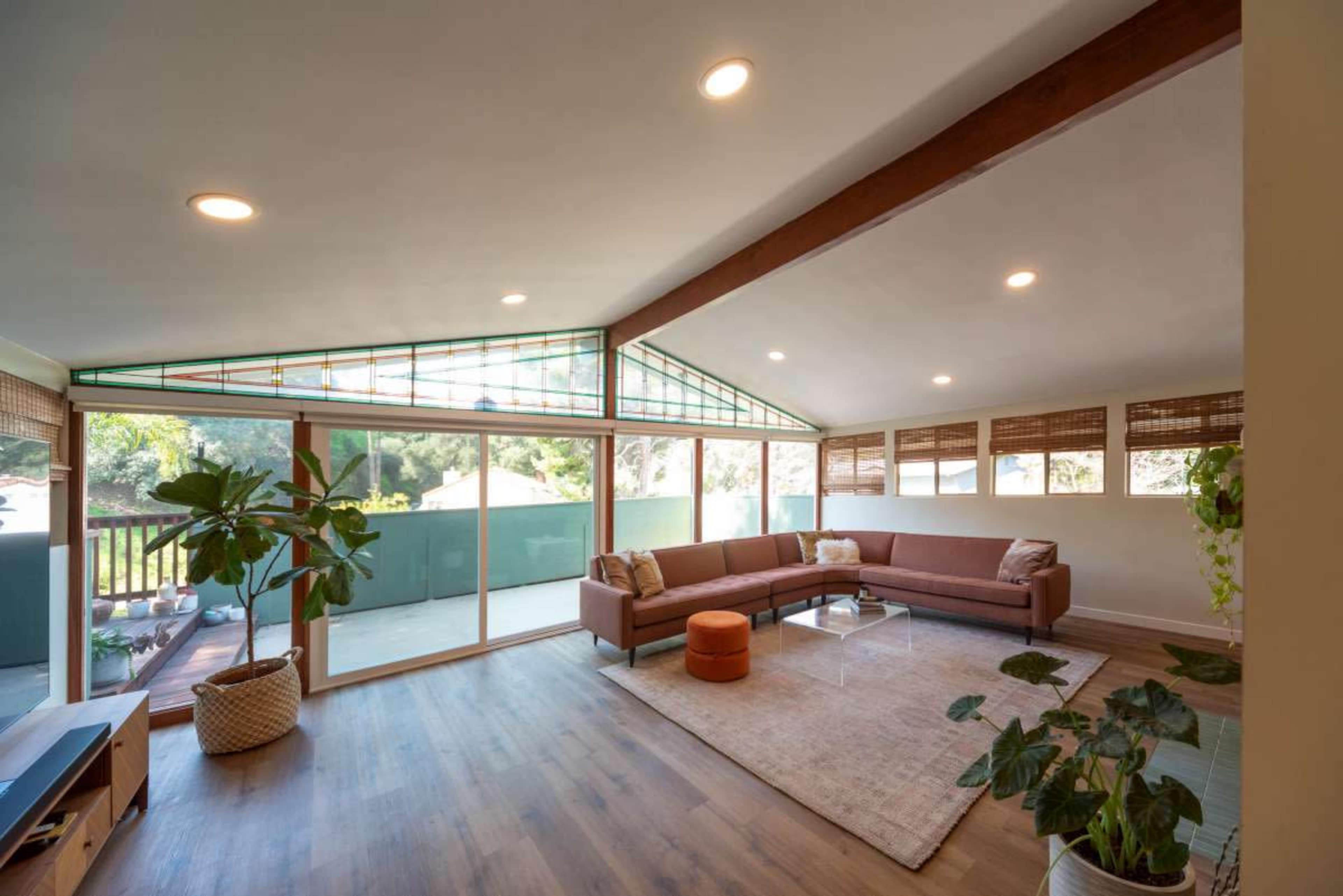 A spacious living room featuring a brown sectional sofa, a glass coffee table, hardwood flooring, and large windows letting in natural light.
