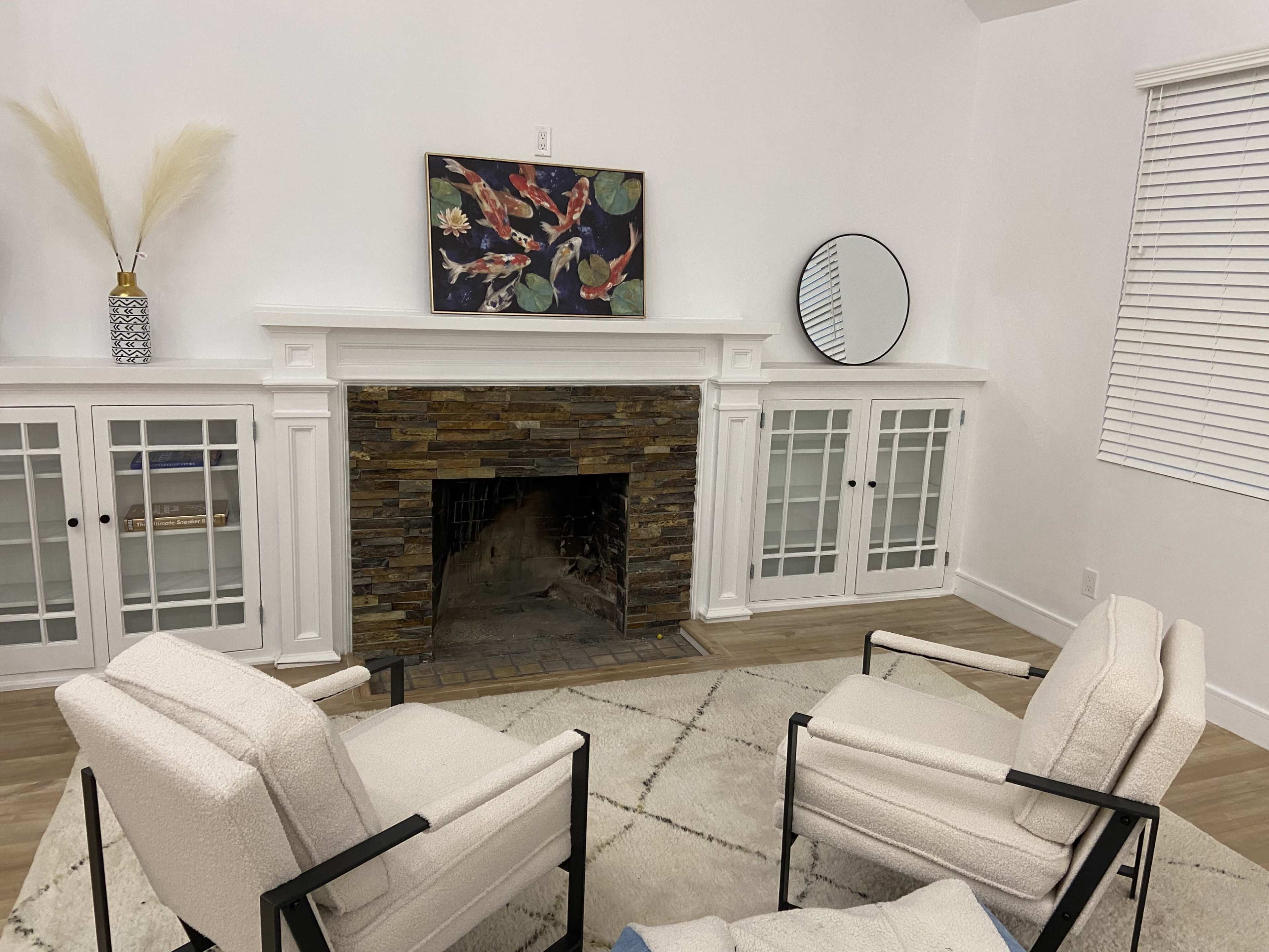 A living room with a stone fireplace, two armchairs facing each other, and a decorative piece hanging above the mantel.
