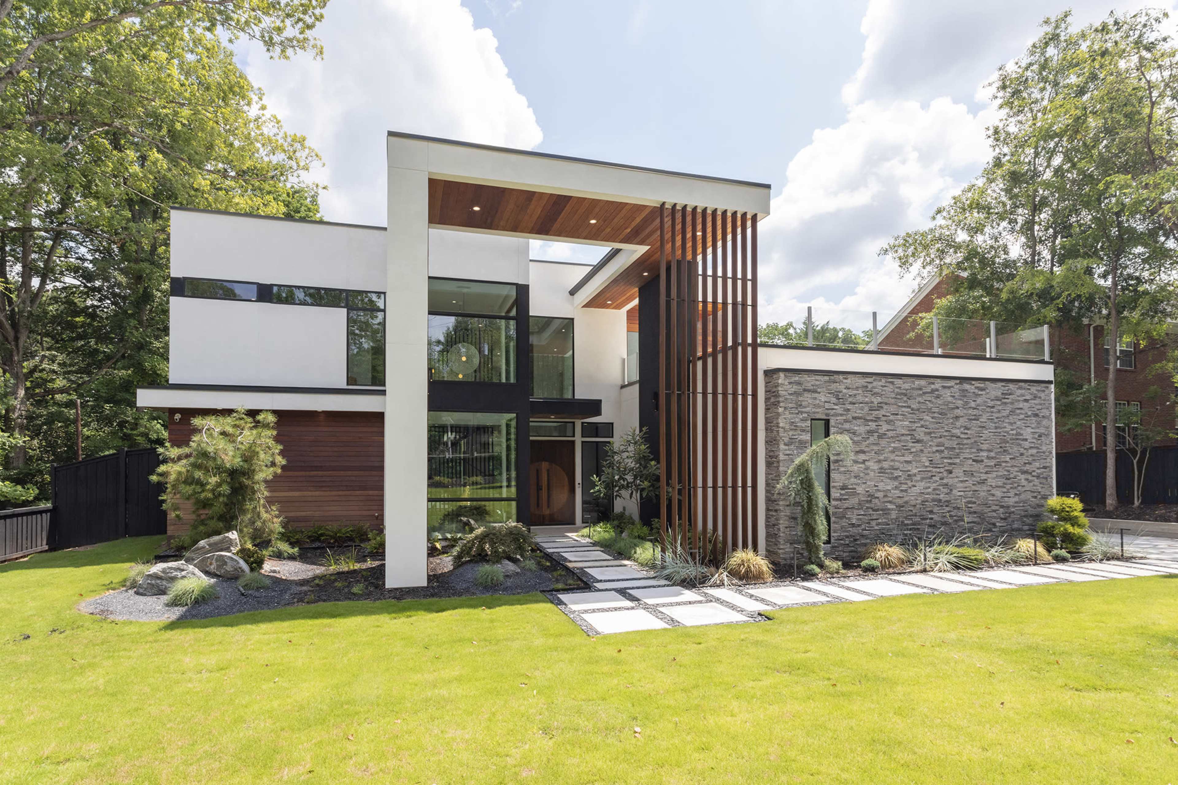 A modern house featuring a combination of wood, stone, and glass elements, with a landscaped front yard and a large entryway.
