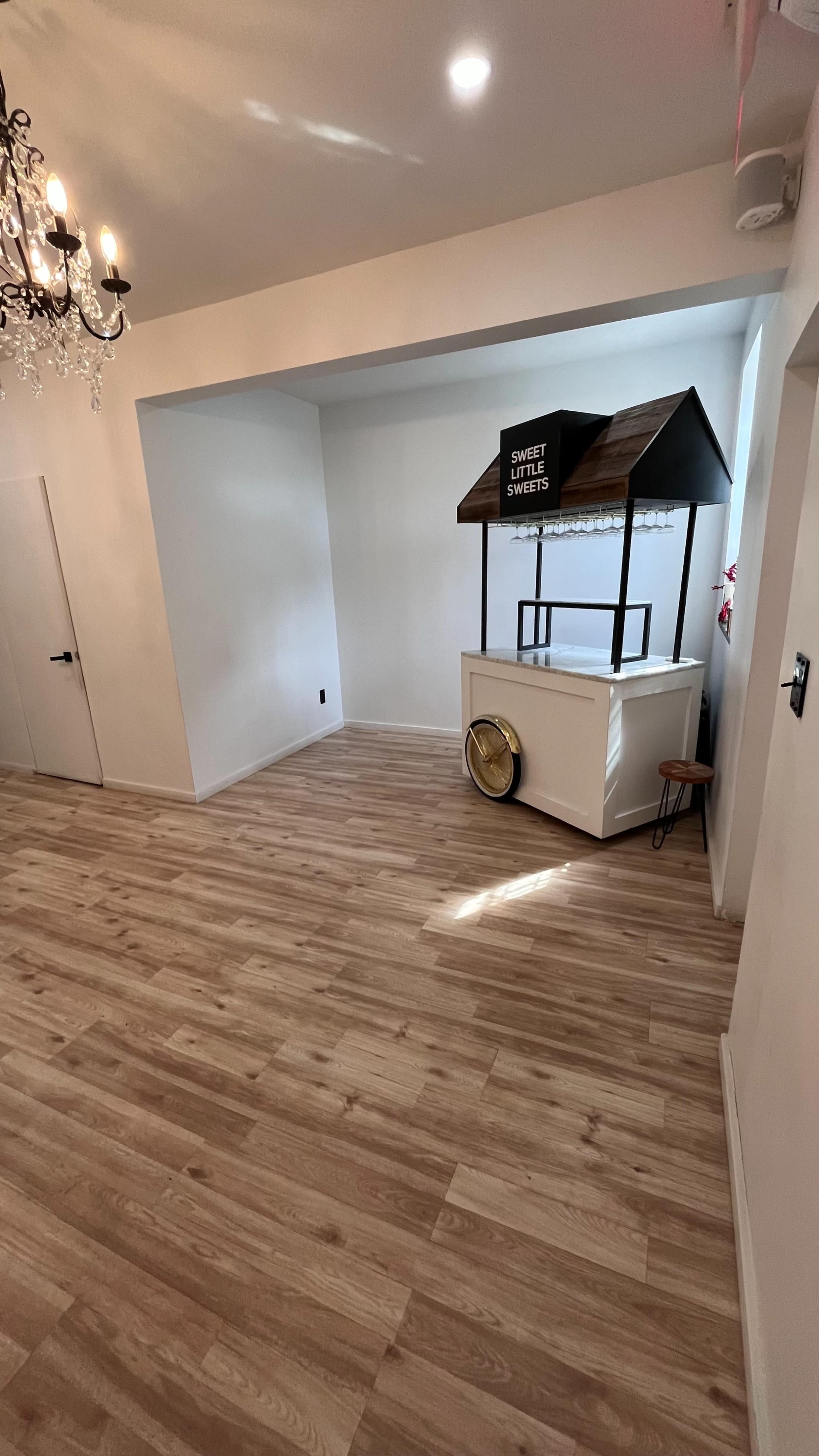A spacious room with light wood flooring, featuring a decorative stand labeled "Sweet Sweets" against a plain wall.