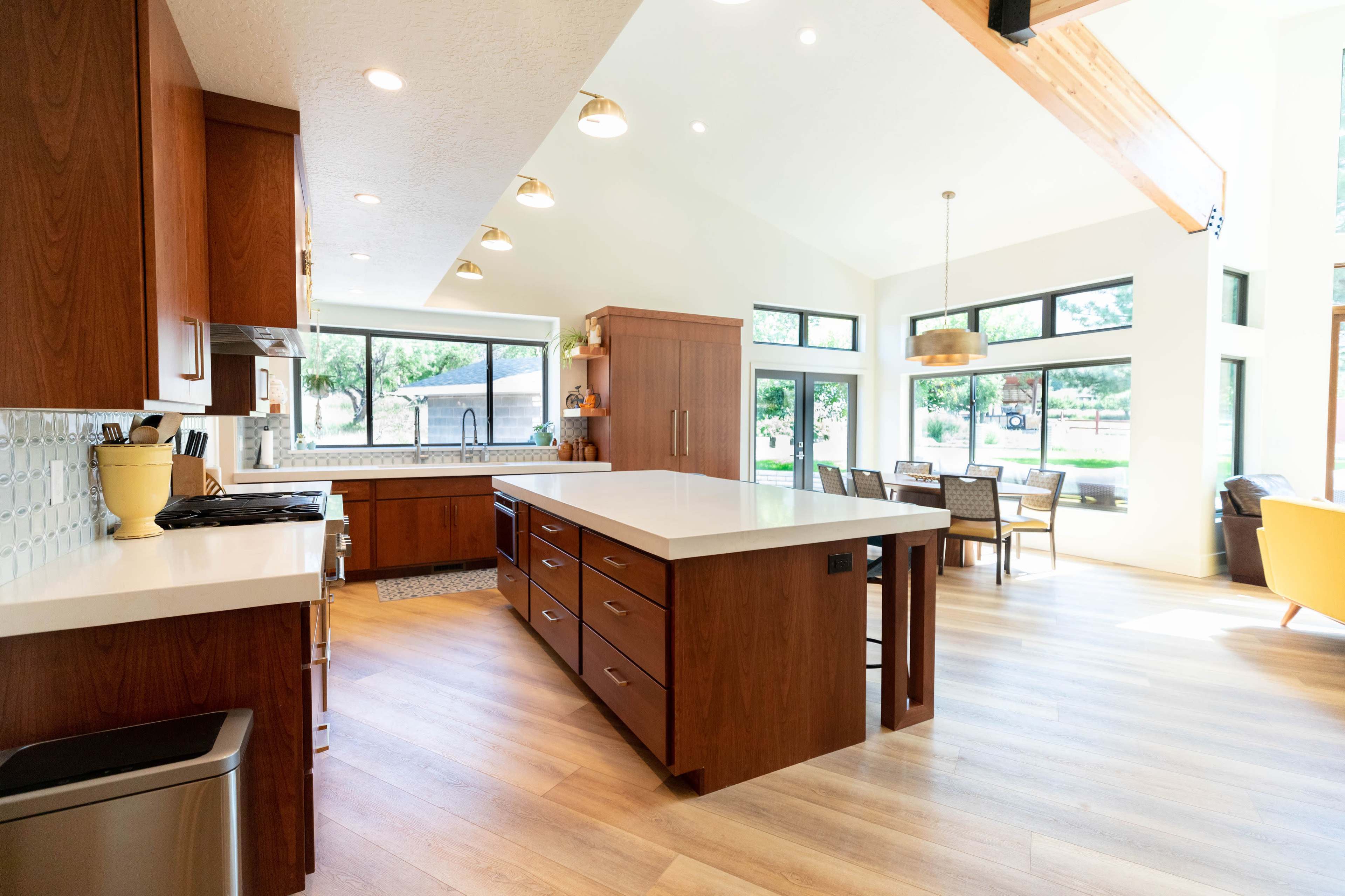 A spacious kitchen with a large island, modern cabinetry, and an adjacent dining area featuring a table and chairs, illuminated by natural light from large windows.